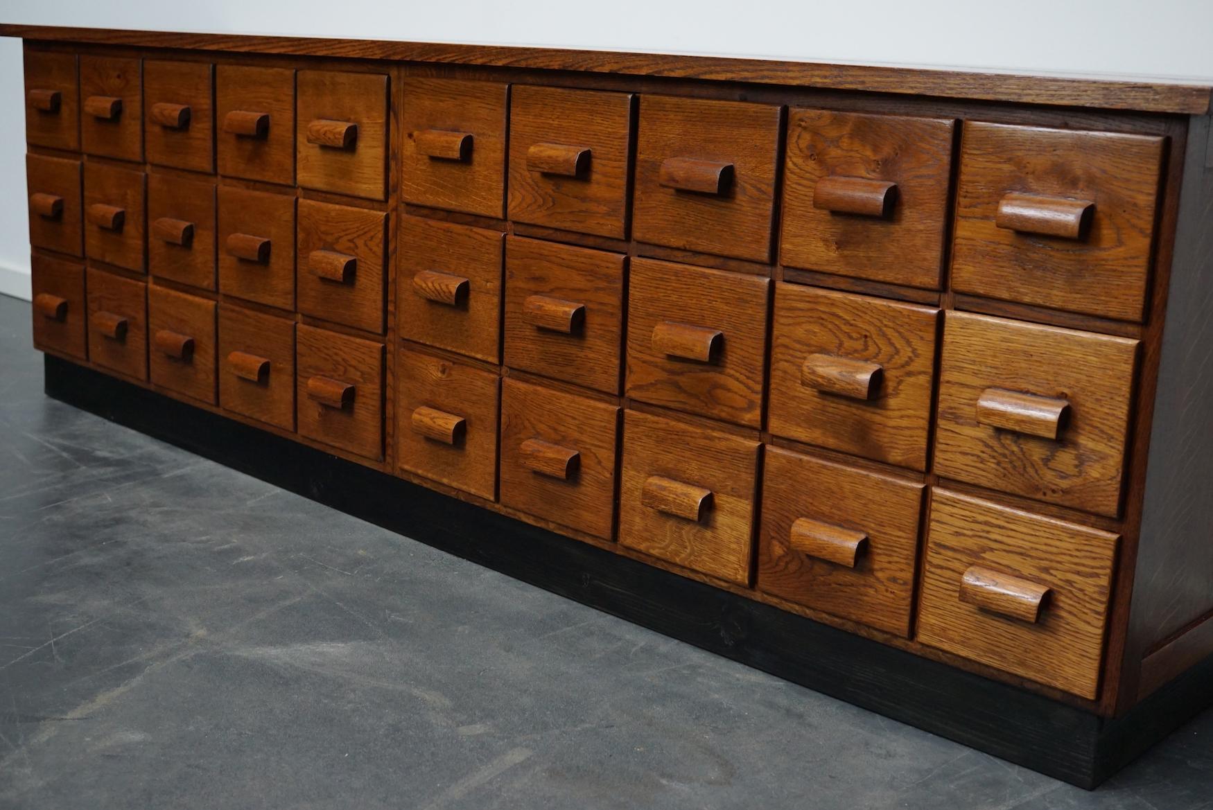 This apothecary cabinet was made circa 1940s in Germany. It features 30 drawers with oak handles. The interior dimensions of the drawers are: D x W x H 33 x 15.5 x 13 cm.