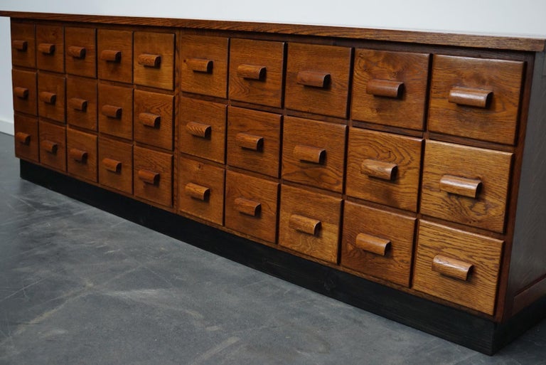 This apothecary cabinet was made circa 1940s in Germany. It features 30 drawers with oak handles. The interior dimensions of the drawers are: D x W x H 33 x 15.5 x 13 cm.