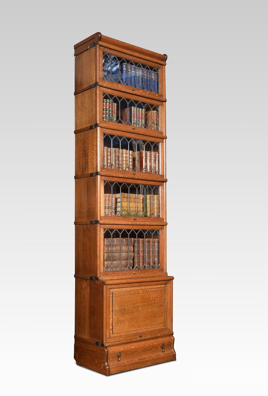 Oak six section bookcase of narrow proportions, the moulded top above five section fitted with leaded glazed doors the base section fitted with a panelled door. All raised up on a plinth base with single long draw.
Dimensions
Height 86.5
