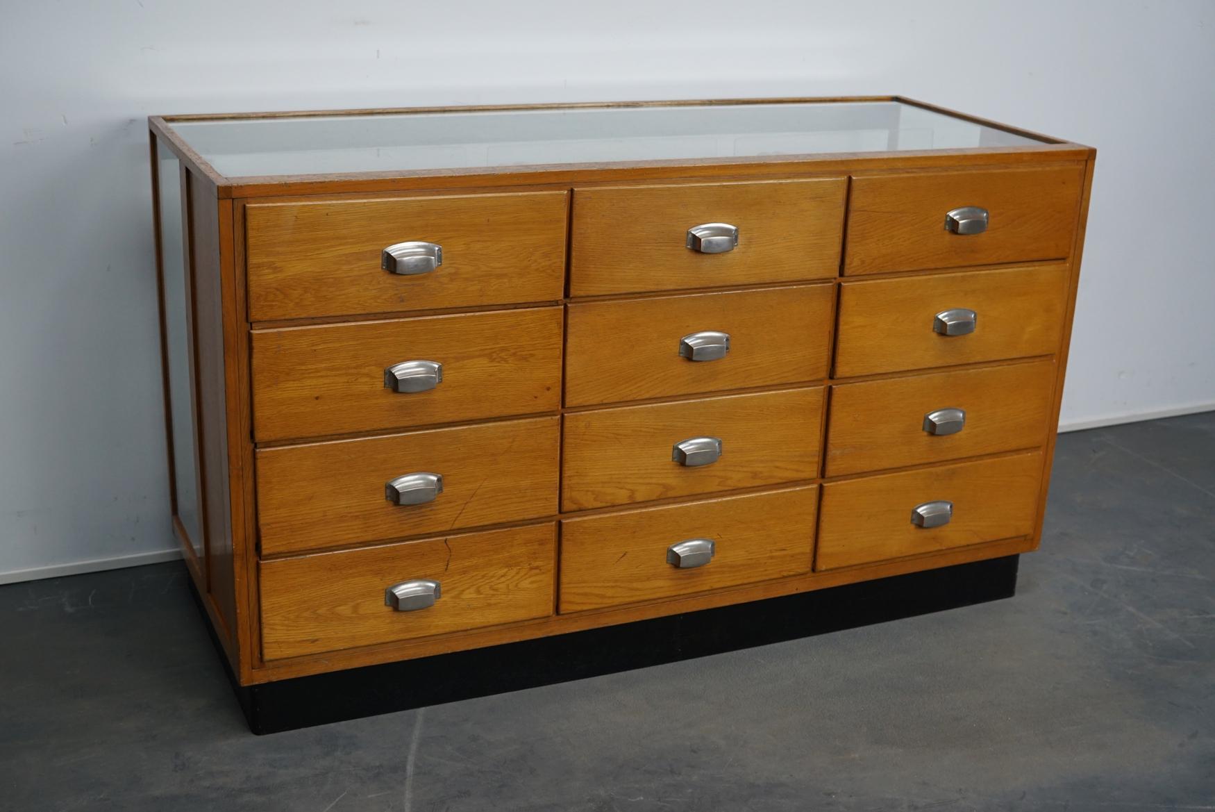 This shop counter was made and manufactured during the 1950s in Germany. It features an oak frame with oak drawers with metal cup handles and a glass casing. It remains in a good vintage condition with some marks consistent with age and use.