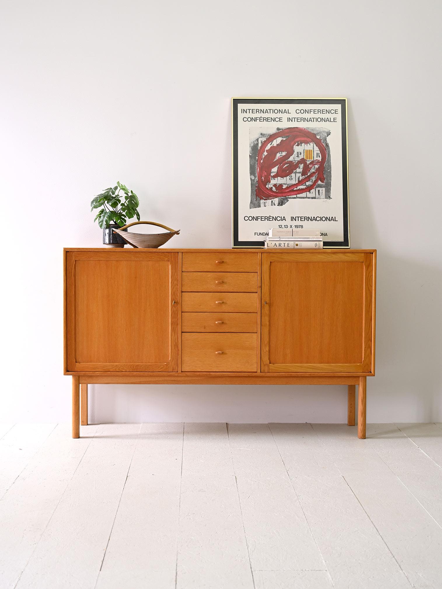 Scandinavian-made highboard manufactured in 1962 in Sweden by the Bodafors company.

The frame is made of oak wood and features five central drawers while on the sides are two lockable hinged doors that conceal two compartments with shelves.

The
