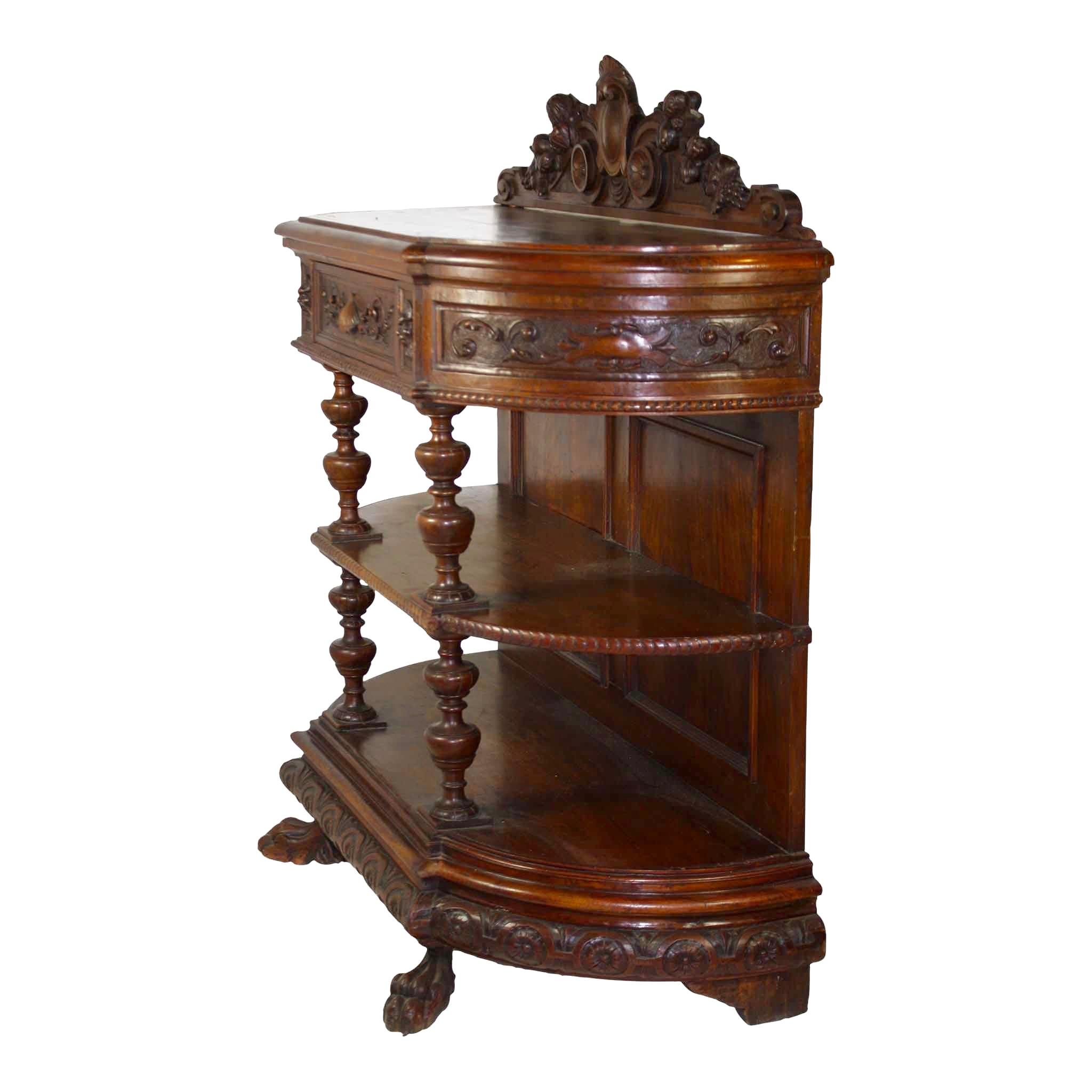 Comprised of solid oak and oak veneer, this beautiful hunt server features graceful lines apparent in the rounded curves of its three tiers, turned risers, and scrolled carvings. The scalloped backboard showcases carved fruit amid foliage with a