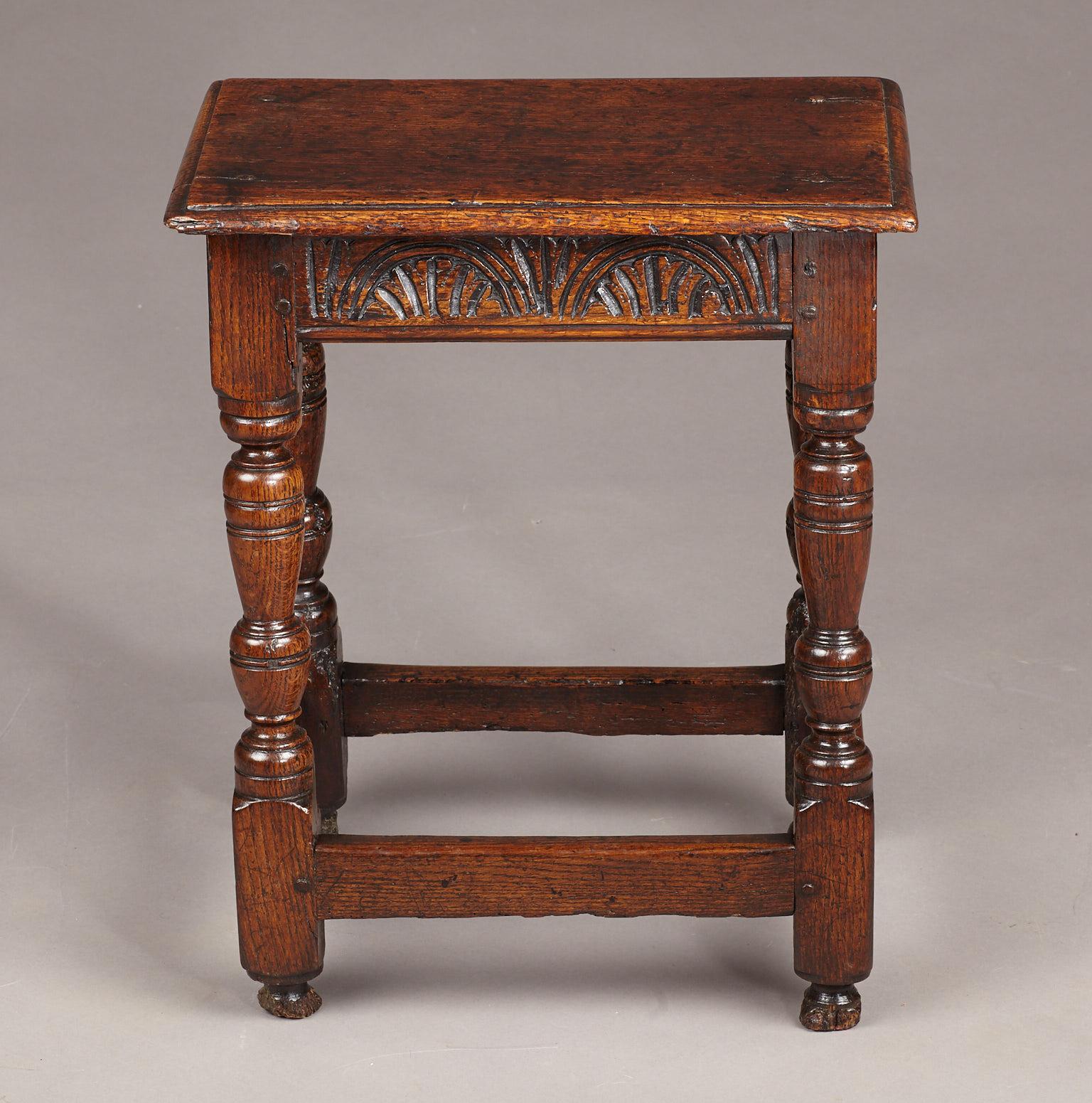 Charles I Oak Joined Stool, Gloucestershire, circa 1630-1640.

The moulded plank top above tapered baluster cup and cover turned legs joined by lunette carved frieze rails, with plain stretchers and remainder of original turned toes.