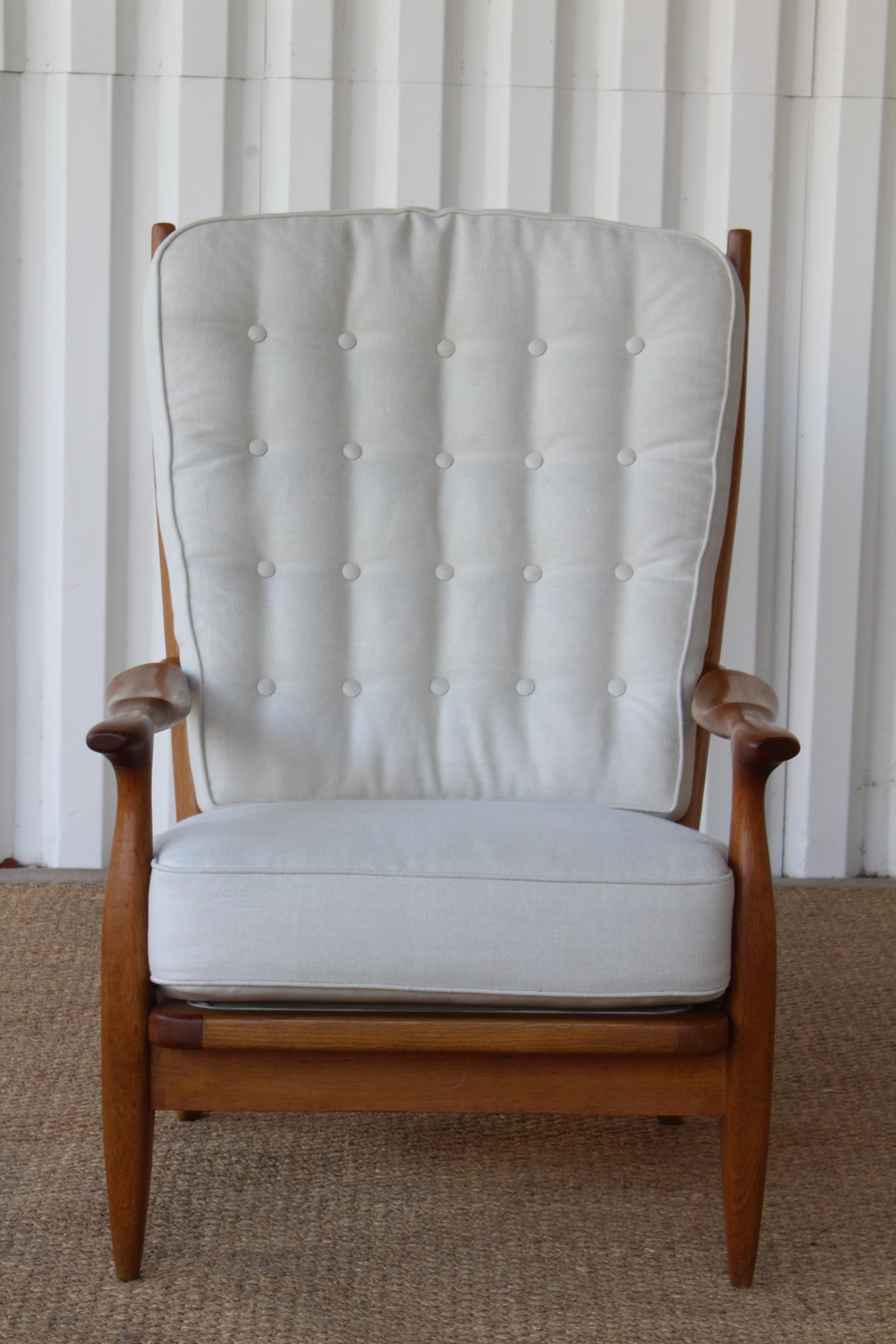 Vintage lounge chair designed by Guillerme et Chambron, France, 1960s. The solid oak frame has been refinished and completed with new cushions upholstered in an off-white Belgian linen. In overall excellent condition with new straps under the seat
