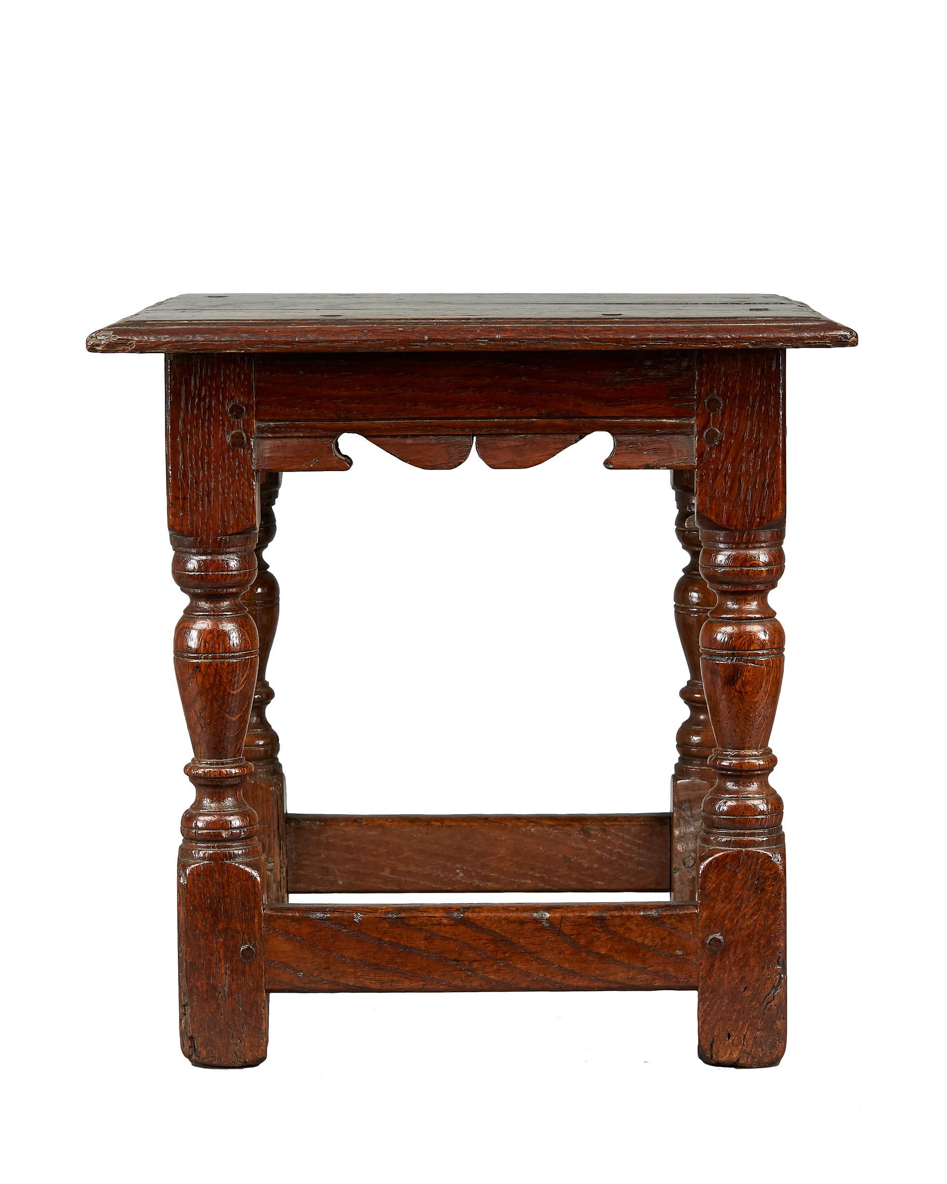 James I / Charles I oak low stool, English, circa 1620-1630.

The eight peg moulded plank top above channel moulded frieze rails with silhouette carved scrolls, joined by inverted baluster and collar turned legs with chamfered stretchers.
