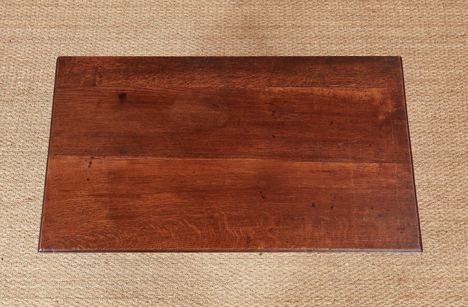 A side table or lowboy with tailored lines in nicely figured oak, having a molded edge top over three beaded drawers with brass bail handles on an apron featuring an open scroll and corner brackets above straight square section legs with grooved