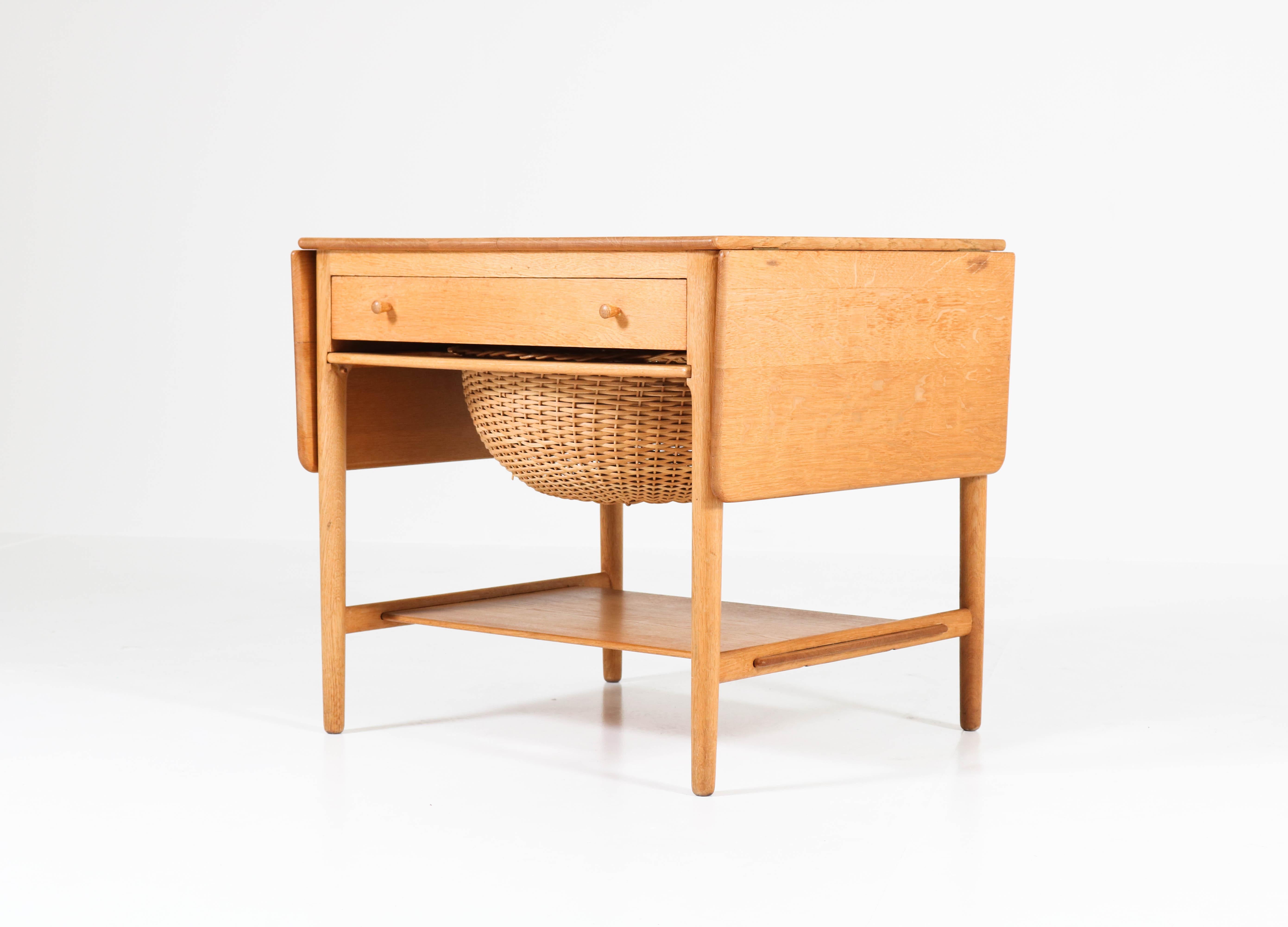 Stunning Mid-Century Modern sewing table model: AT-33.
Design by: Hans J Wegner for Andreas Tuck.
Striking Danish design from the 1950s.
Solid oak base with original storage basket and drawer.
Tabletop can be extended with two drop
