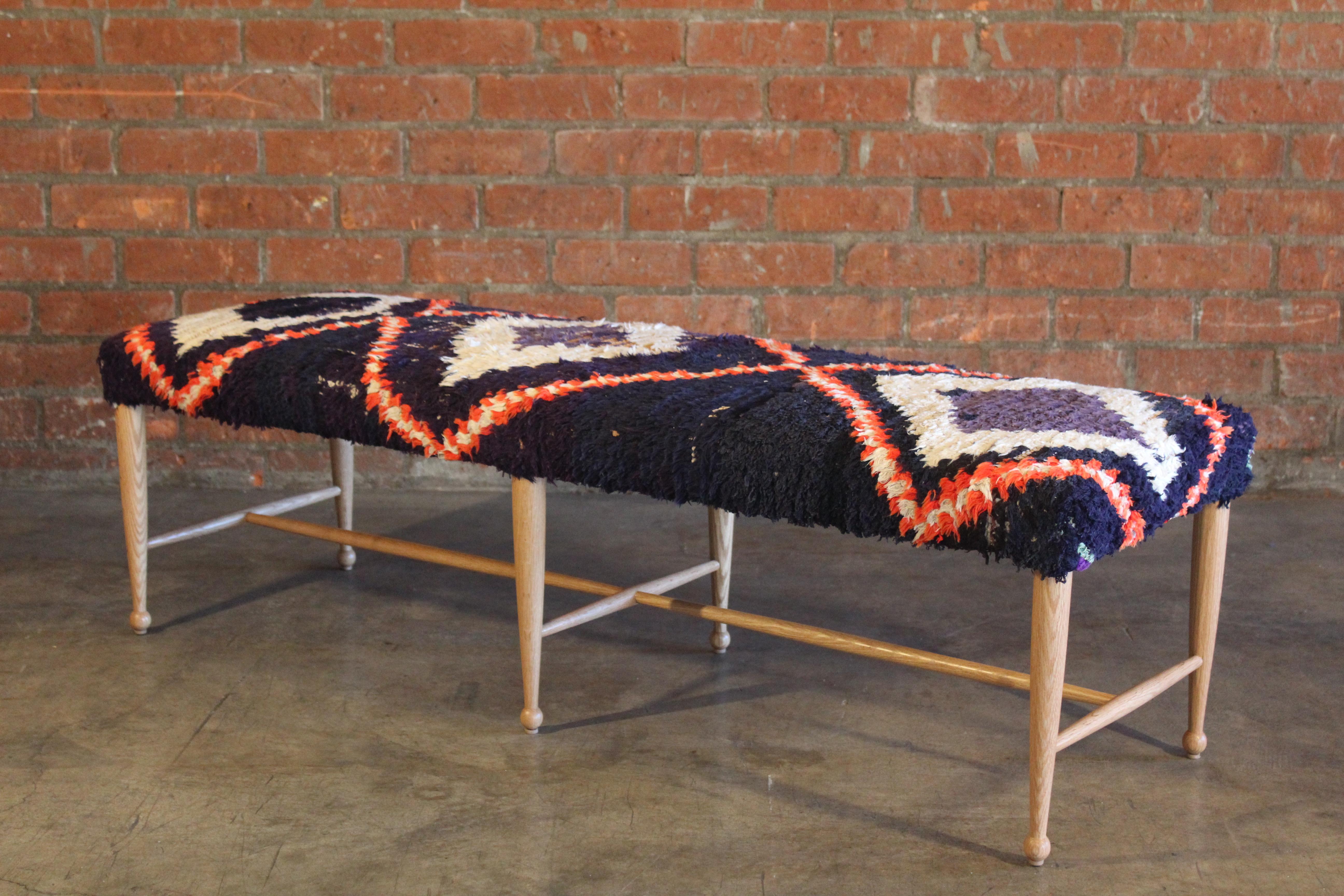 A vintage inspired bench with mid-century lines upholstered in a vintage 1960s Moroccan rug. Hand crafted in Los Angeles with a solid oak base in a natural finish. The rug used was professionally cleaned and may show signs of wear.