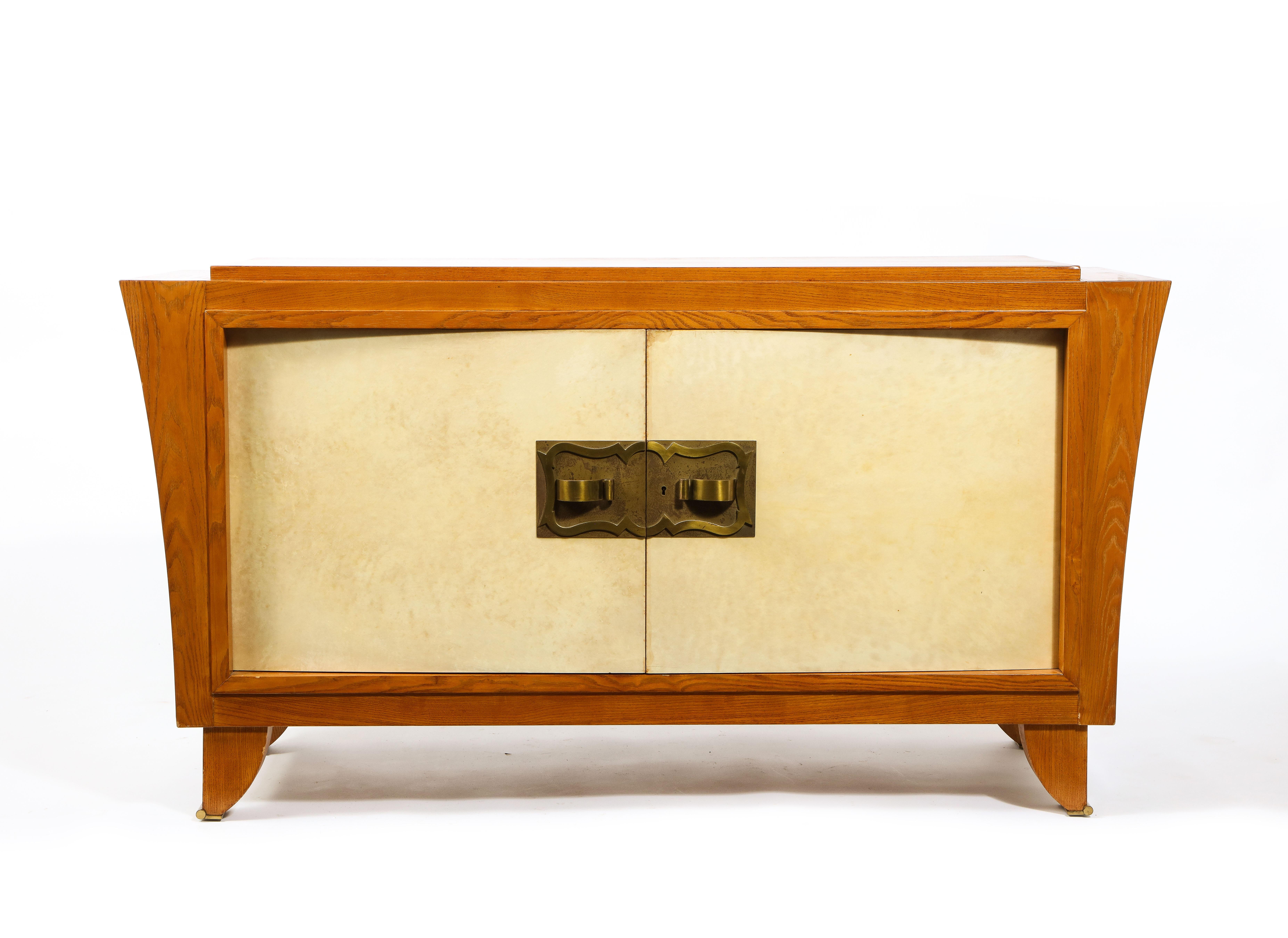 Elegant two-door parchment & oak cabinet with bronze hardware. The sides flare out as they go upwards and the top is recessed. The body rests on four elegant feet finished with bronze sabots. The narrow long drawers are ideal for storing linens or
