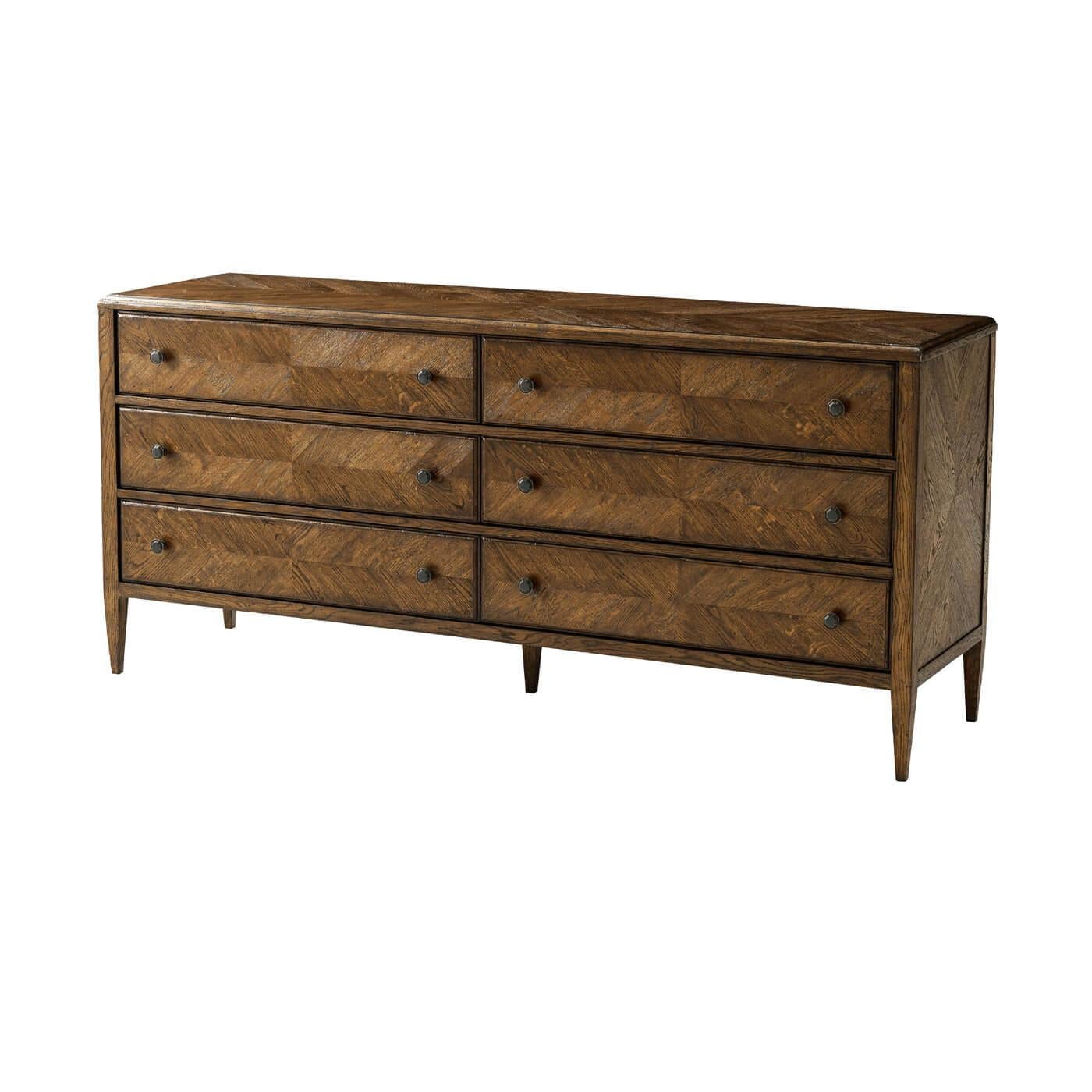 A dark oak parquetry six-drawer dresser in Dusk finish. This beautiful hand-carved oak dresser includes six drawers with mirrored herringbone starburst parquetry finished with Verde Bronze handles on classically tapered oak legs. A perfect dresser
