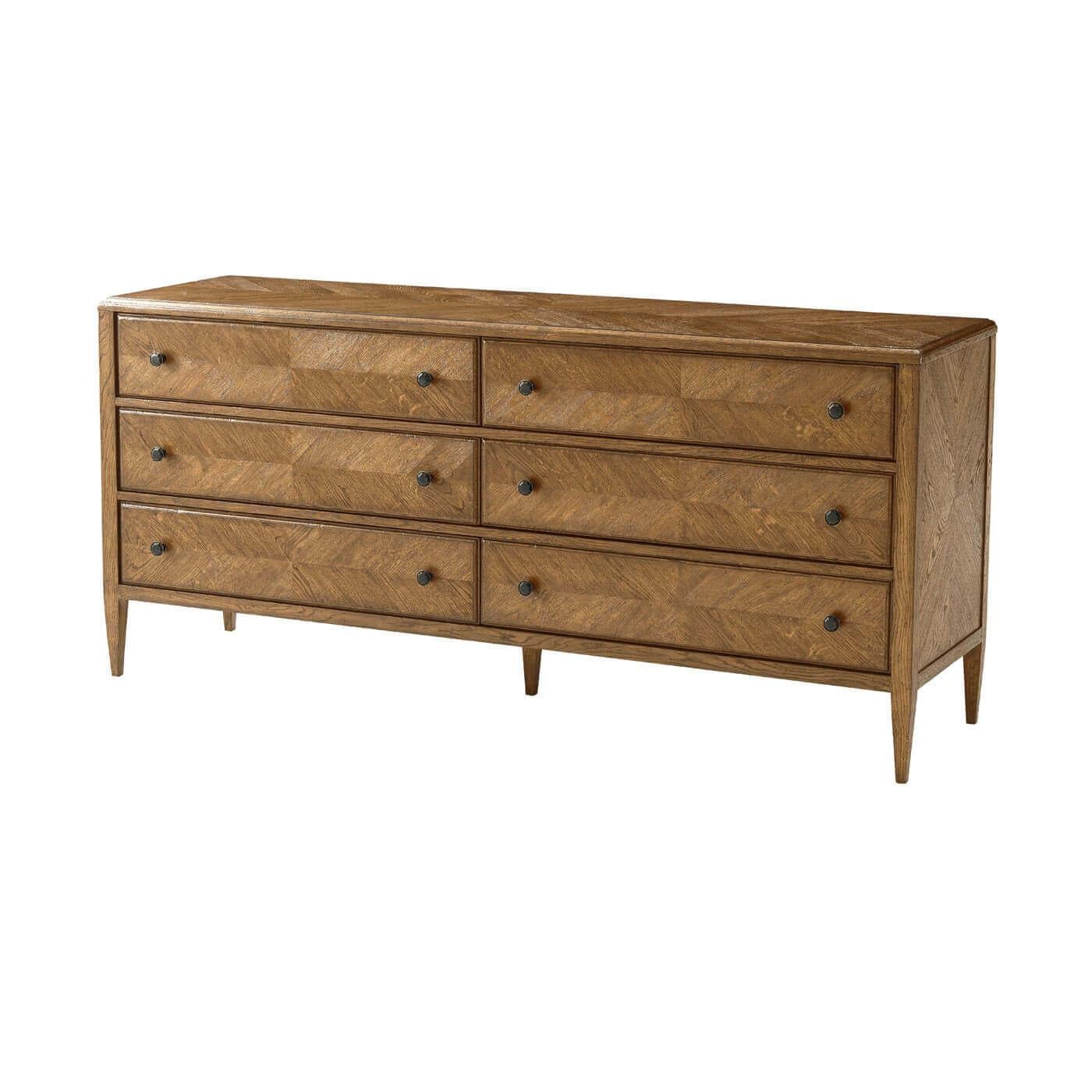A light oak parquetry six-drawer dresser in dawn finish. This beautiful hand-carved oak dresser includes six drawers with mirrored herringbone starburst parquetry finished with Verde Bronze handles on classically tapered oak legs. A perfect dresser
