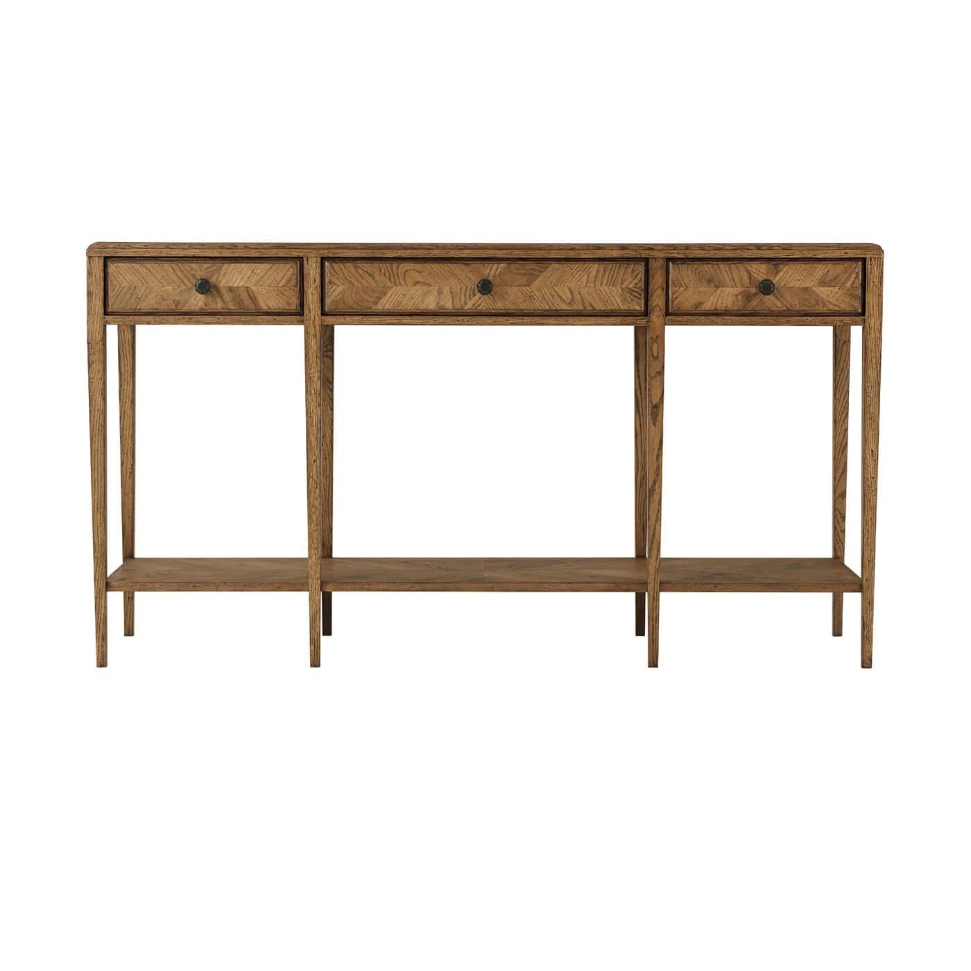An oak parquetry two-tier console table with mirrored herringbone oak parquetry on its top and drawer faces. This two-tiered table includes three frieze drawers accented with Verde Bronze finished handles and has solid tapered legs. It is shown in