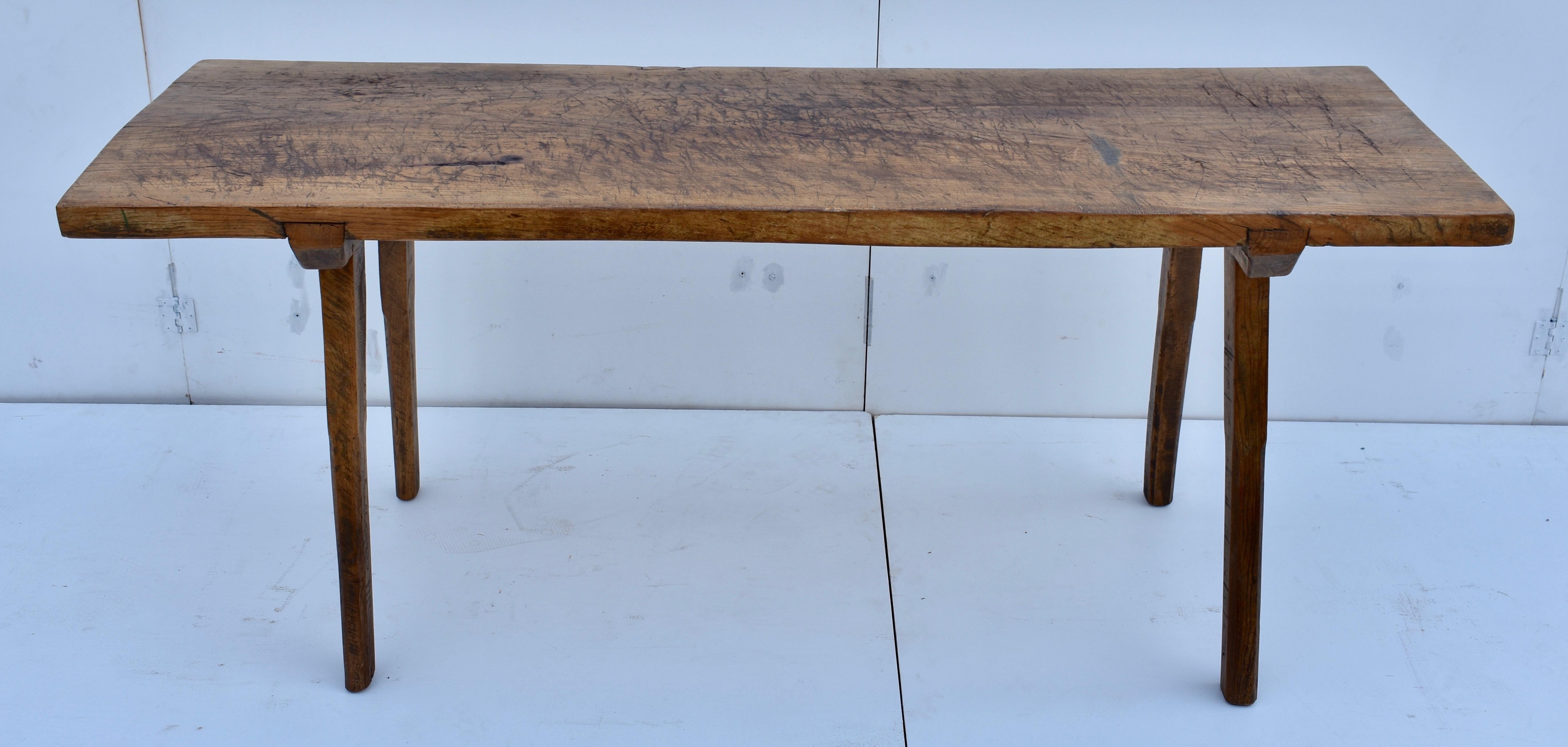 The top of this magnificent pig bench table is a single massive slab of oak, almost six feet long and two feet wide. It is beautifully chopped and gnarled after decades of purposeful use. The splayed legs are 2” square at the top and further down