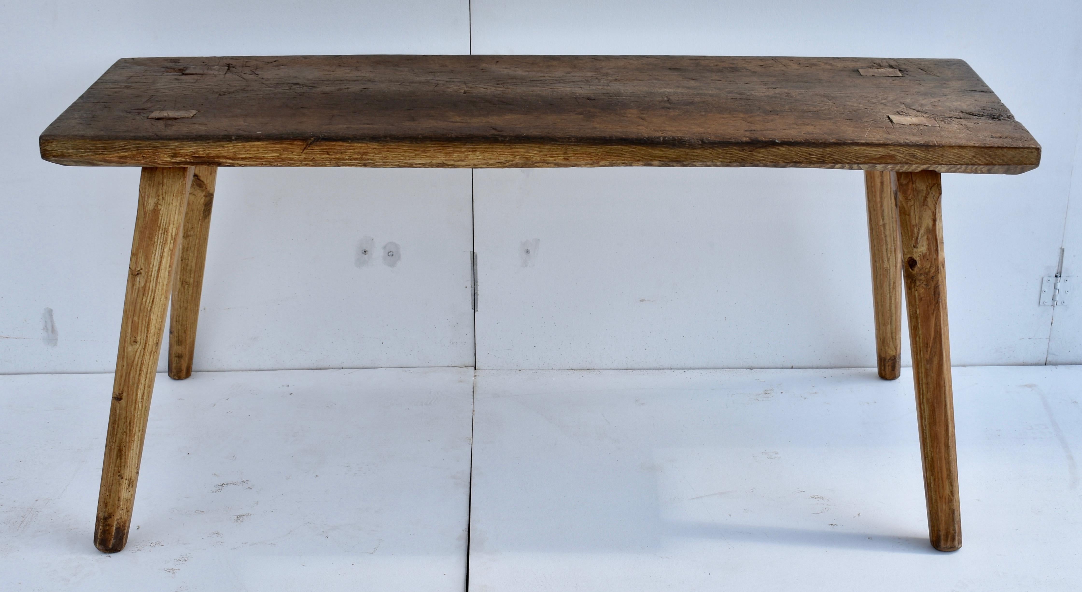 The top of this massive Pig Bench is a single slab of oak 2.5” thick, well-worn through decades of purposeful use and partially chamfered on its lower edge. The splayed square legs, tenoned all the way through the top and tightened with wedges, are