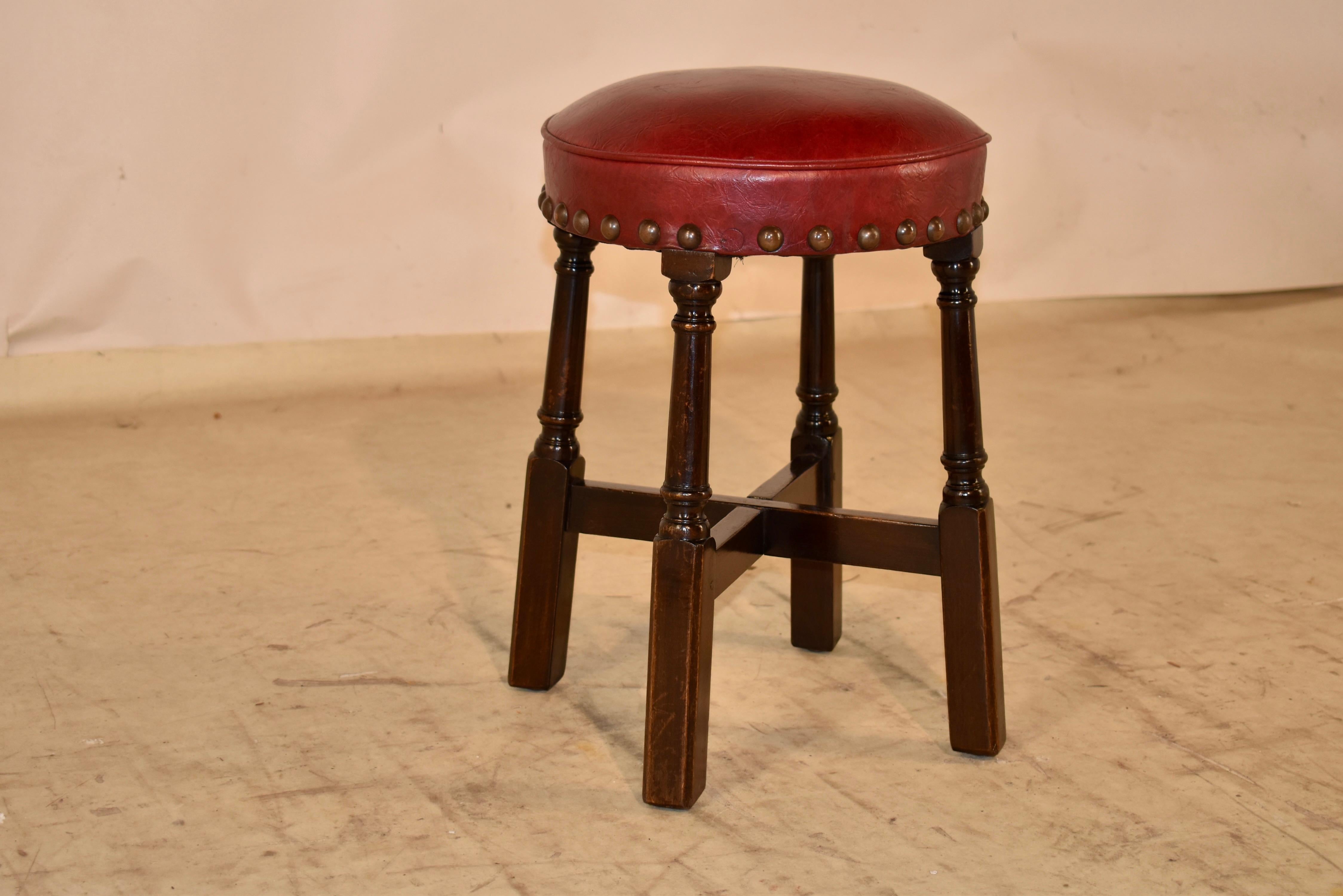 Charming 1920's pub stool from England.  The seat is upholstered in what appears to be faux leather in a rich red color and finished around the base of the seat with brass tacks.  The base of the stool has nicely turned and slightly splayed legs,