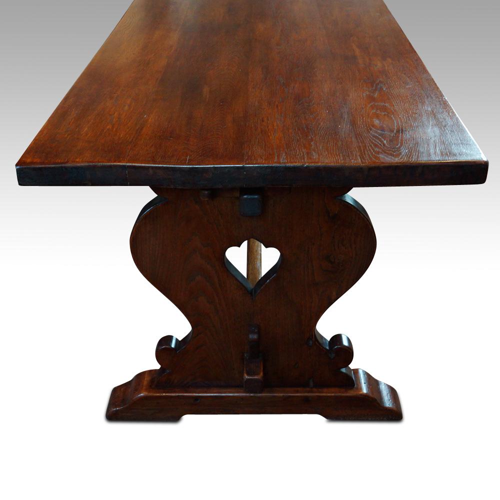 This oak refectory dining table was made, circa 1920.
The table with a 4 cms (1 1/4ins) solid top, and the base with trestle silhouette supports joined by an upper and lower stretcher that are secured by pegs that tap into place. This makes the