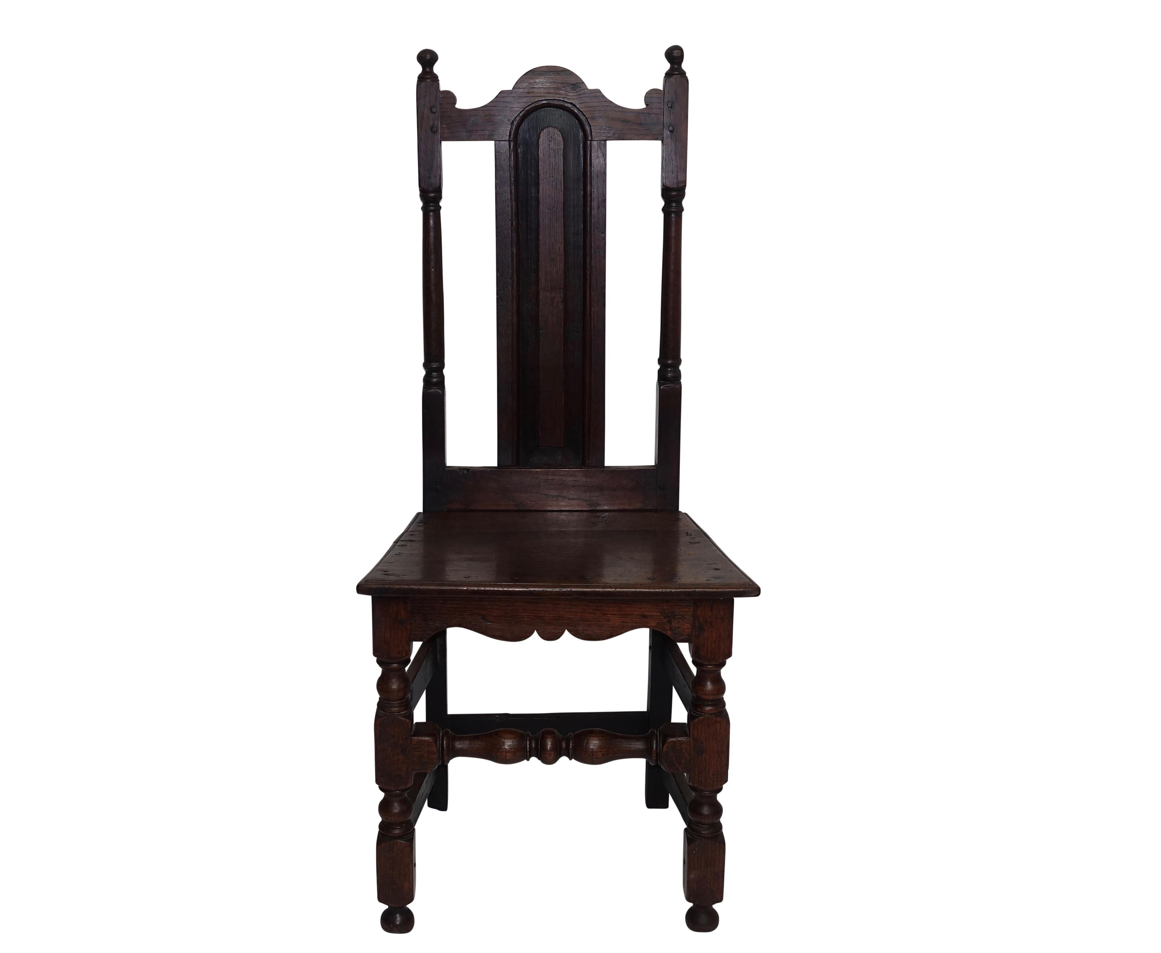 Oak side chair with panel back splat and arched top rail, having a plank seat above two turned front legs and shaped apron. Peg and tenon construction, England, circa 1730.