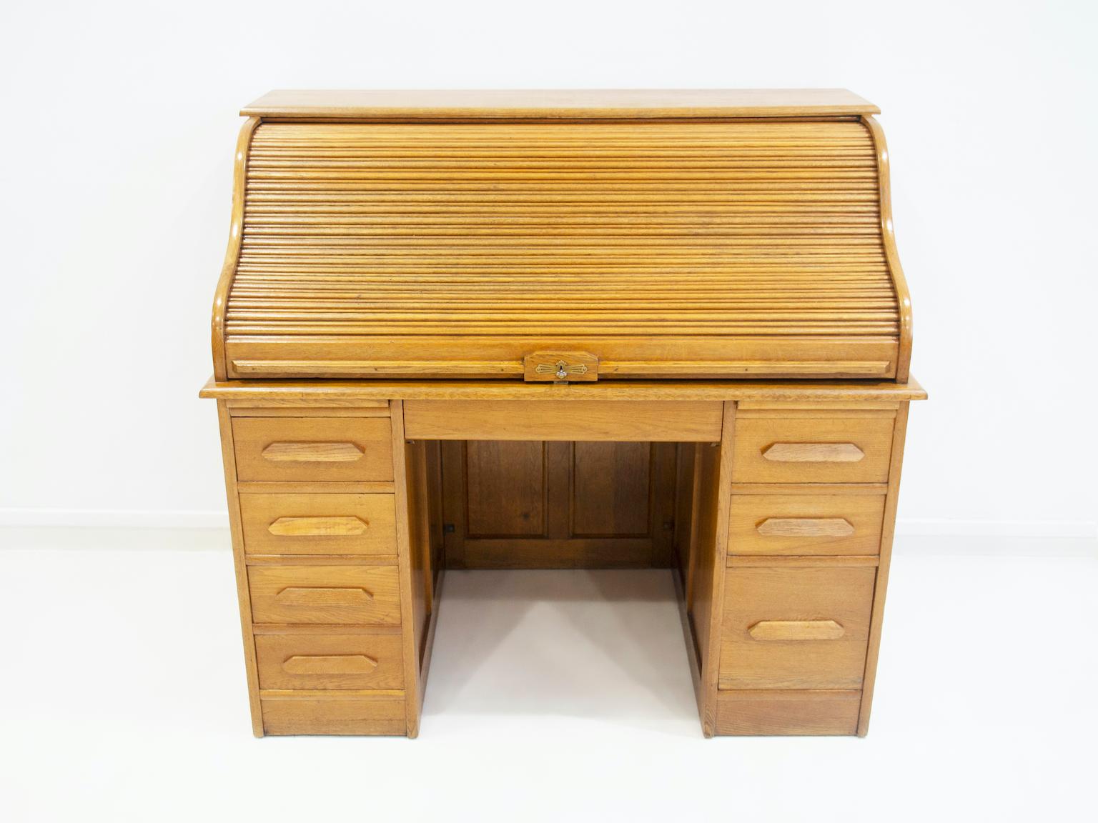 Oak secretaire / writing desk from circa 1900's. Featuring a roll-up flap with underlying writing board, shelf interior and two drawers. Below the writing desk there are two pull-out boards and seven drawers. Key available.