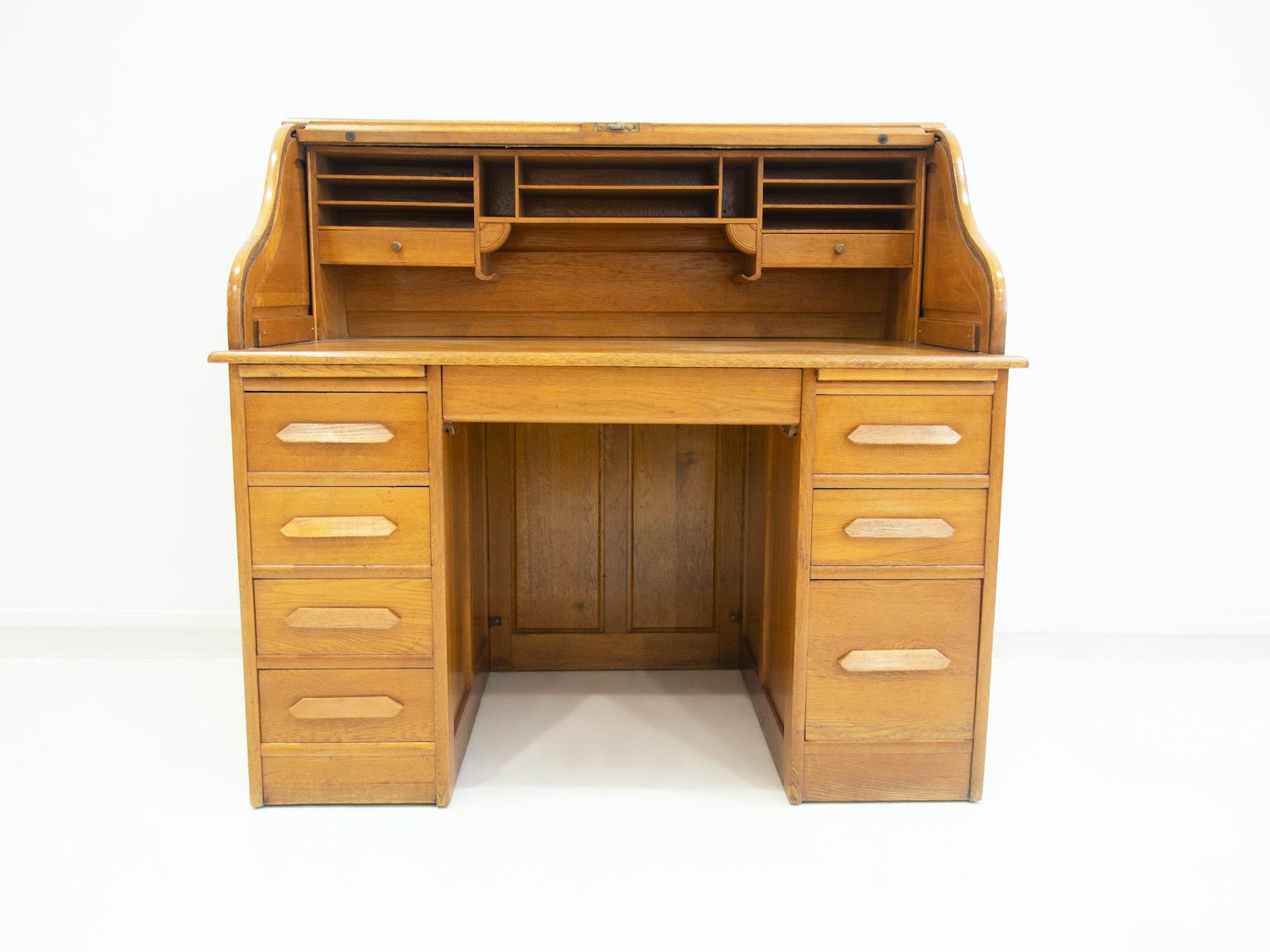 Oak secretary / writing desk from circa 1900's. Featuring a roll-up flap with underlying writing board, shelf interior and two drawers. Below the writing desk there are two pull-out boards and seven drawers. Key available.
