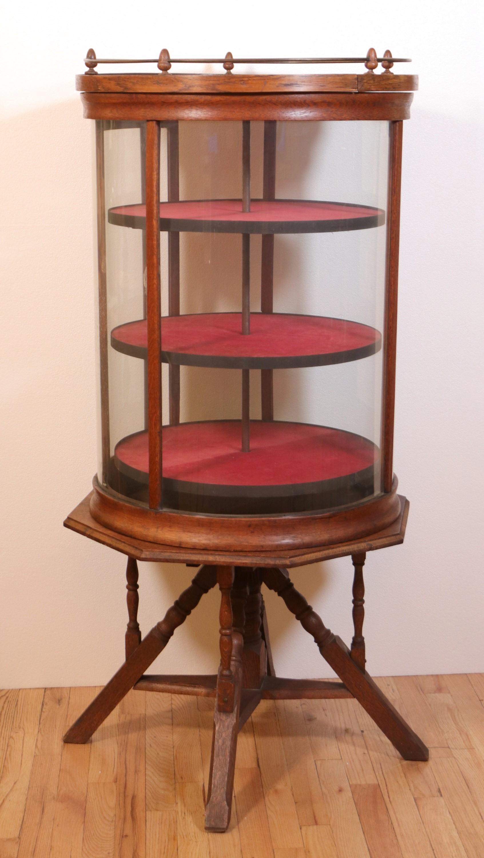 This antique oak revolving display case features three shelves lined with red felt. It has a handsome oak base with spindle type legs. Not only does it have a unique style, but also operates smoothly and has minimal surface wear due to age.