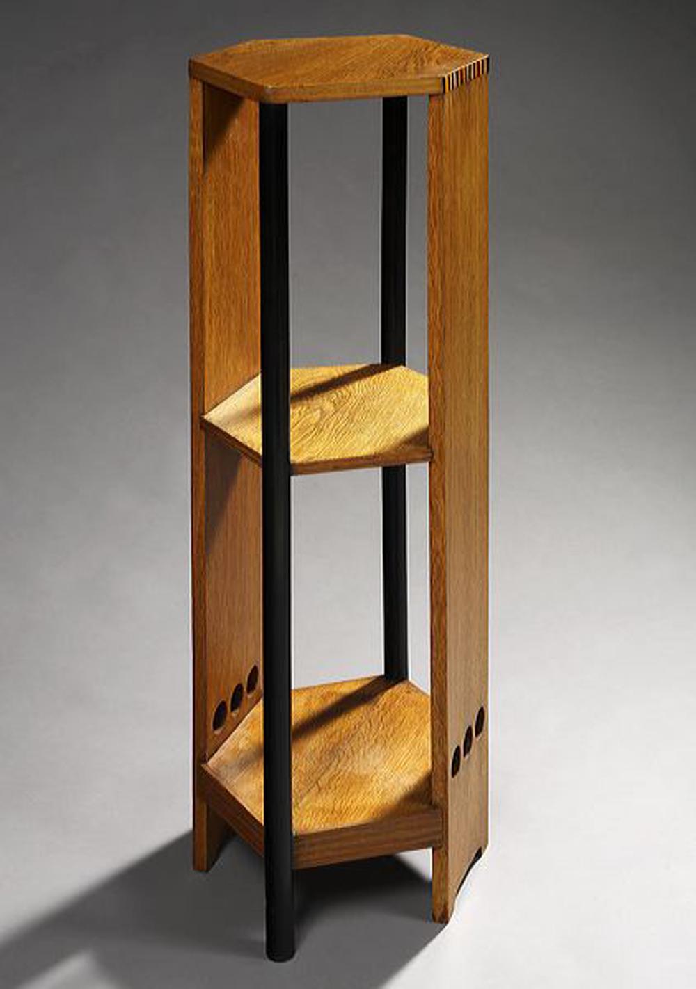 Hexagonal in shape with solid lateral posts decorated at the top with blackened wooden stripes and at the bottom with three open circles.
It is equipped with three shelves connected by two cylindrical uprights also in blackened wood.