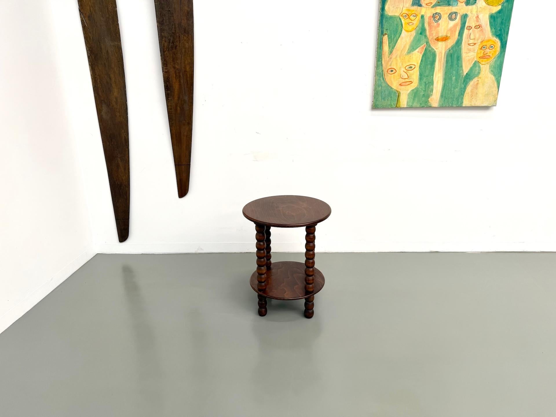 La Maison Lecan presenta un elegante tavolino in rovere tinto scuro attribuito a Charles Dudouyt, circa 1940.

Il design scultoreo è caratterizzato da quattro gambe tornite, emblematiche dello stile rustico ma sofisticato dell'artista.

Il doppio