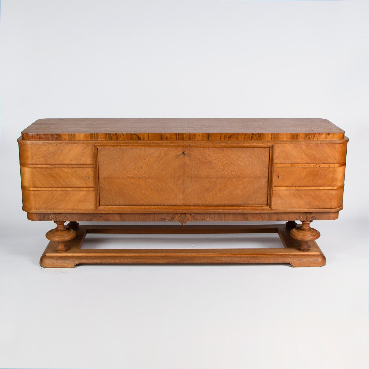 A light oak sideboard, with a carved frieze and turned legs on an open plinth.

Three lockable sections, the central section with a fall front is lined in green felt/baize for storing cutlery.

The felted interior is labelled: NORDEX ST.