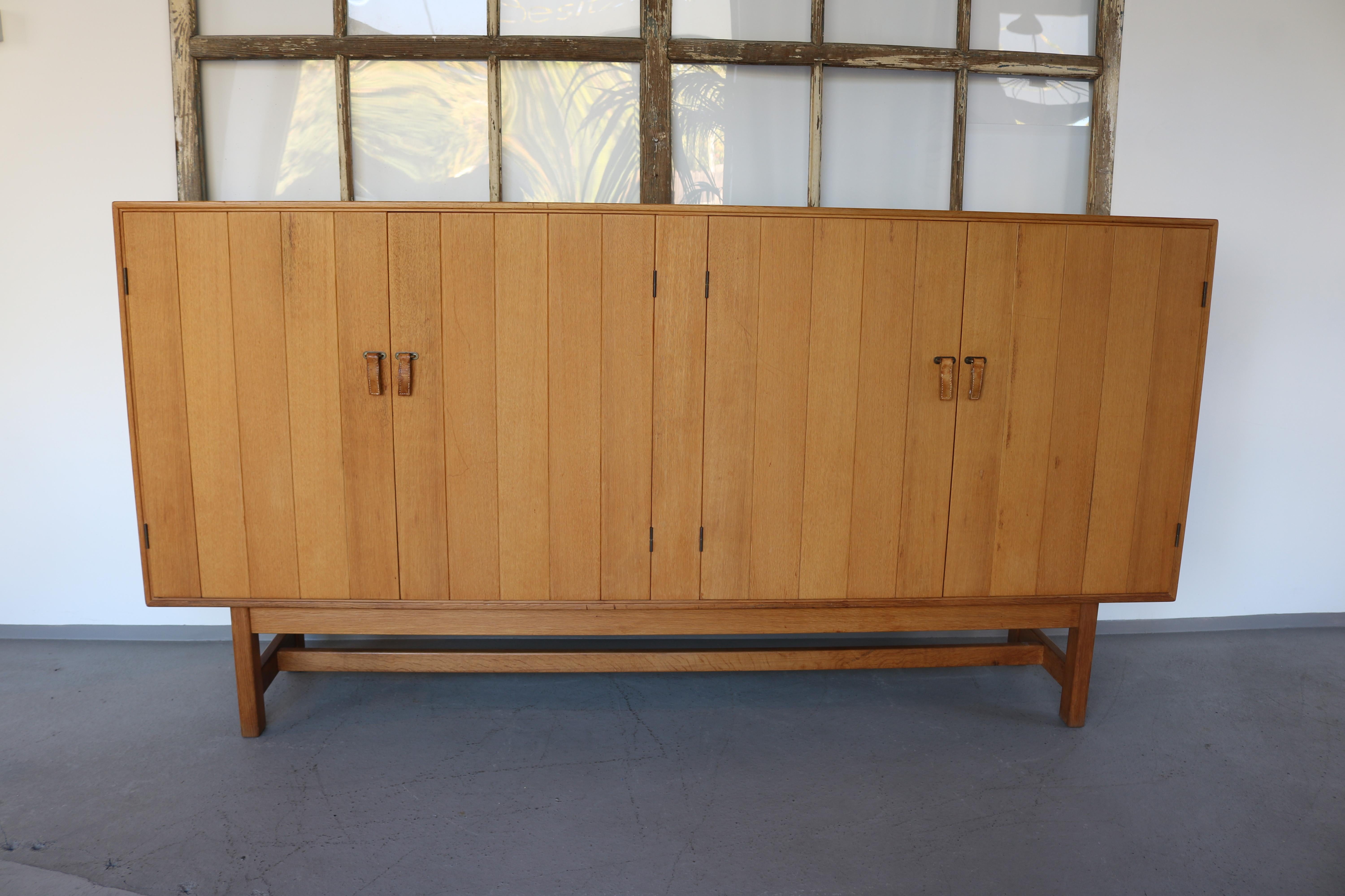 Very rare and exclusive large four-door sideboard in oak, with leather and brass handles.
Danish work by designer Kurt Ostervig, edited by HC Mobler, dating from the 1960s.