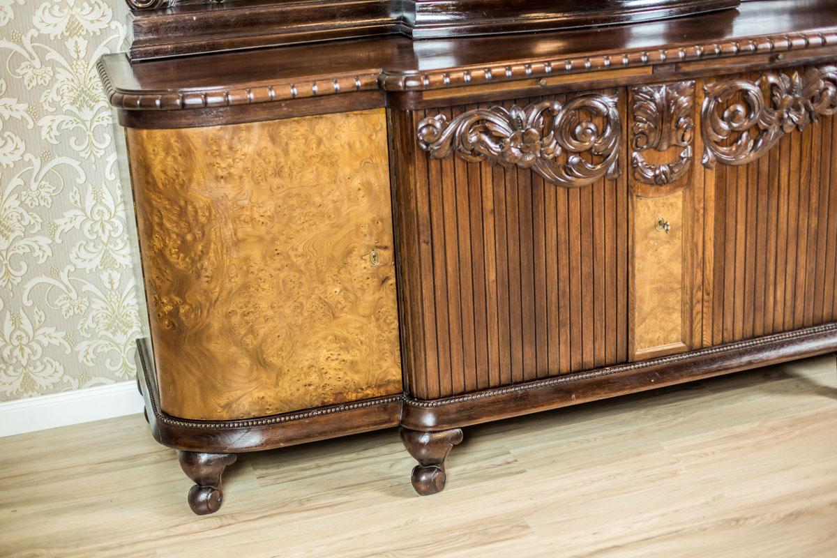 We present you this piece of furniture of a grand size, circa 1918, made of oak.
The top and doors are veneered with oak and walnut burl.
This sideboard is composed of a four-door base and a removable, glazed upper section with semi-round crystal