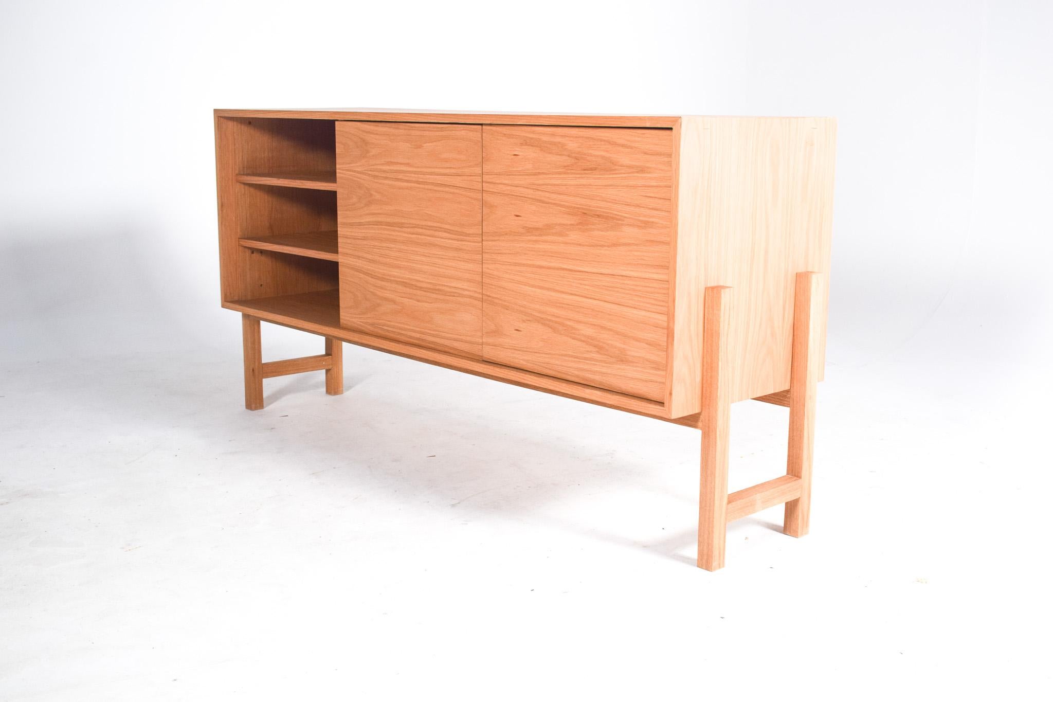 
This modern oak sideboard features a clean and minimalist design that complements a contemporary interior space. The sideboard stands on four sturdy legs that elevate it off the ground, adding to its elegant profile. Its construction boasts a fine