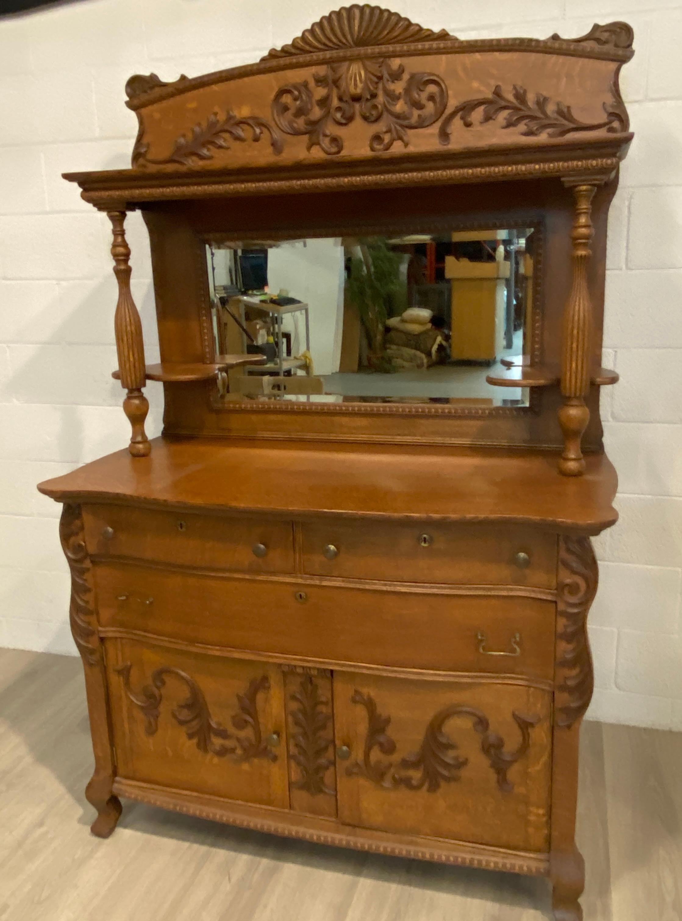Offering here a sideboard with oak solids and quarter cut oak and a beveled glass mirror backing. The carvings are are relief carvings attached in the appropriate scale to enhance the strong character of the oak sideboard.  This sideboard has been