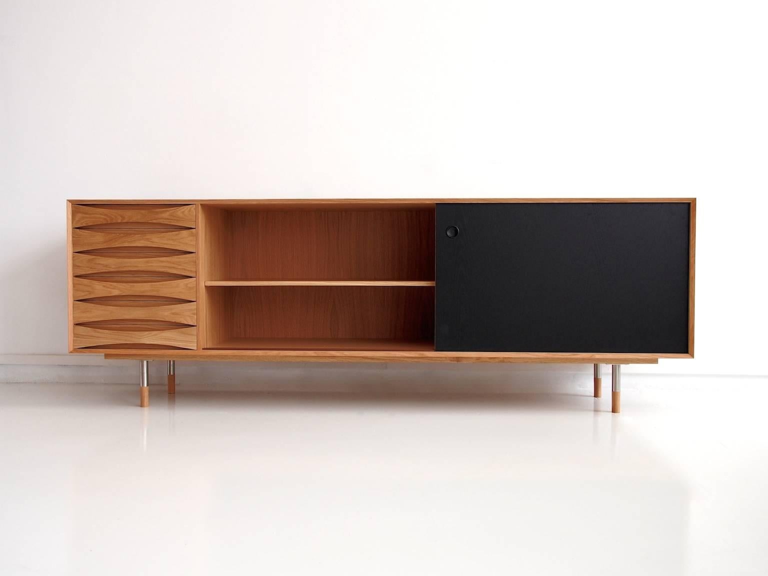 Oil-treated oak sideboard attributed to Arne Vodder. Reversible sliding doors in oak and black varnish. Left side with six drawers. Round steel legs with oak caps.