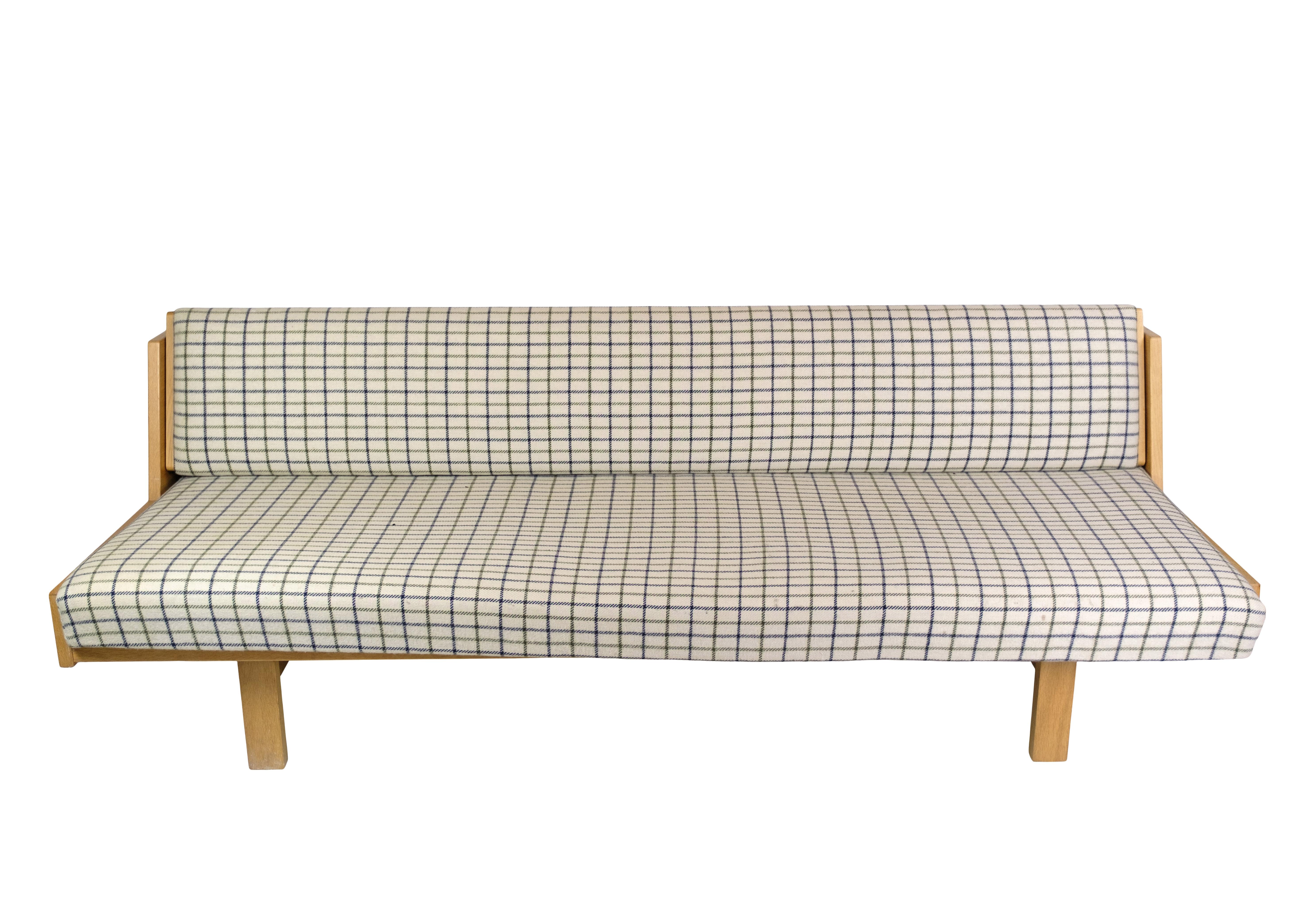 Hans J. Wegner's oak daybed / sofa is a unique design from around the 1960s, created with a timeless aesthetic and manufactured at Getama. It impresses with a nice solid oak frame and light fabric cushions with a charming checkered pattern. The sofa