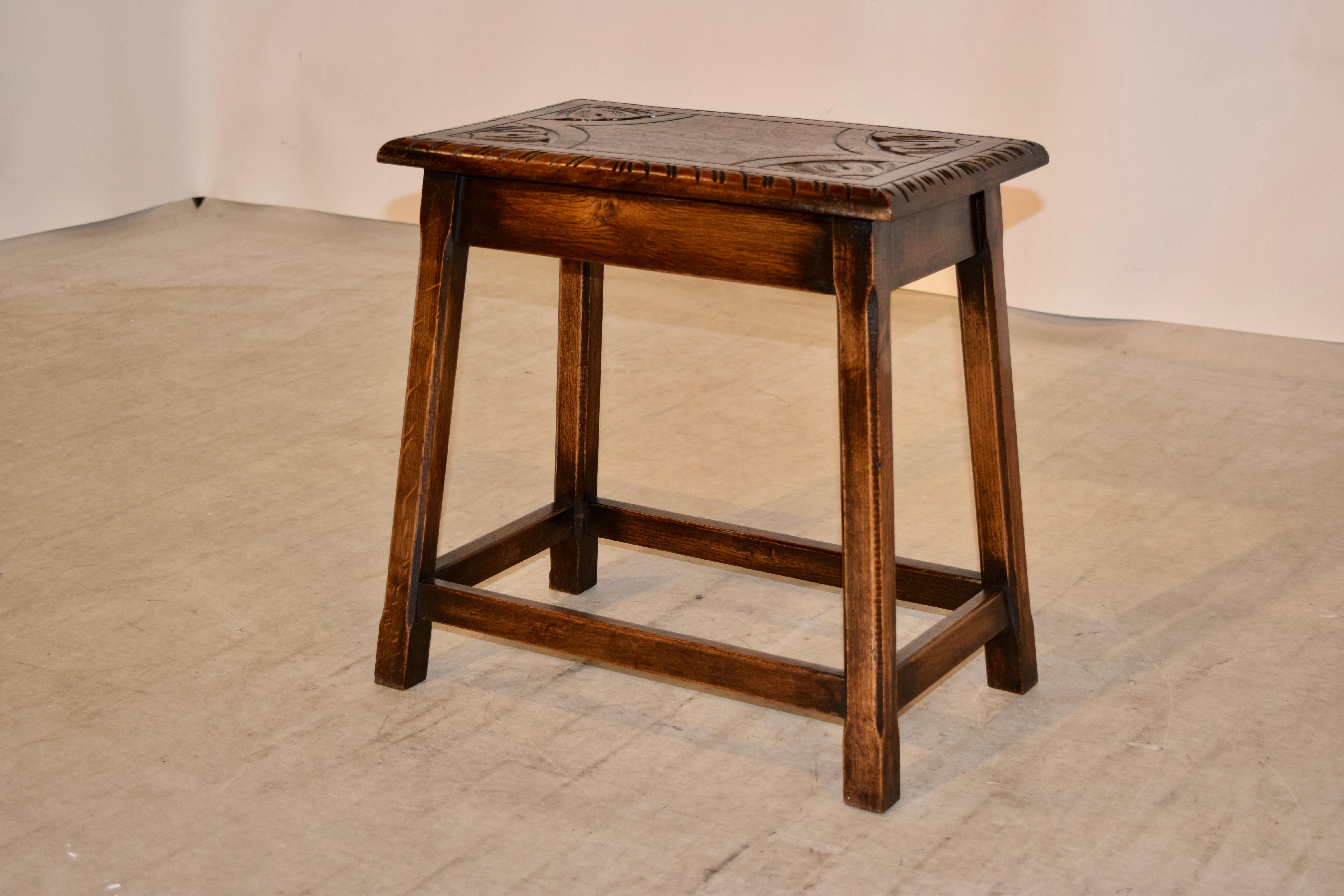 English oak stool circa 1900 with a hand carved decorated top following down to a simple apron and four splayed legs, all with routed corners, joined by simple stretchers.
