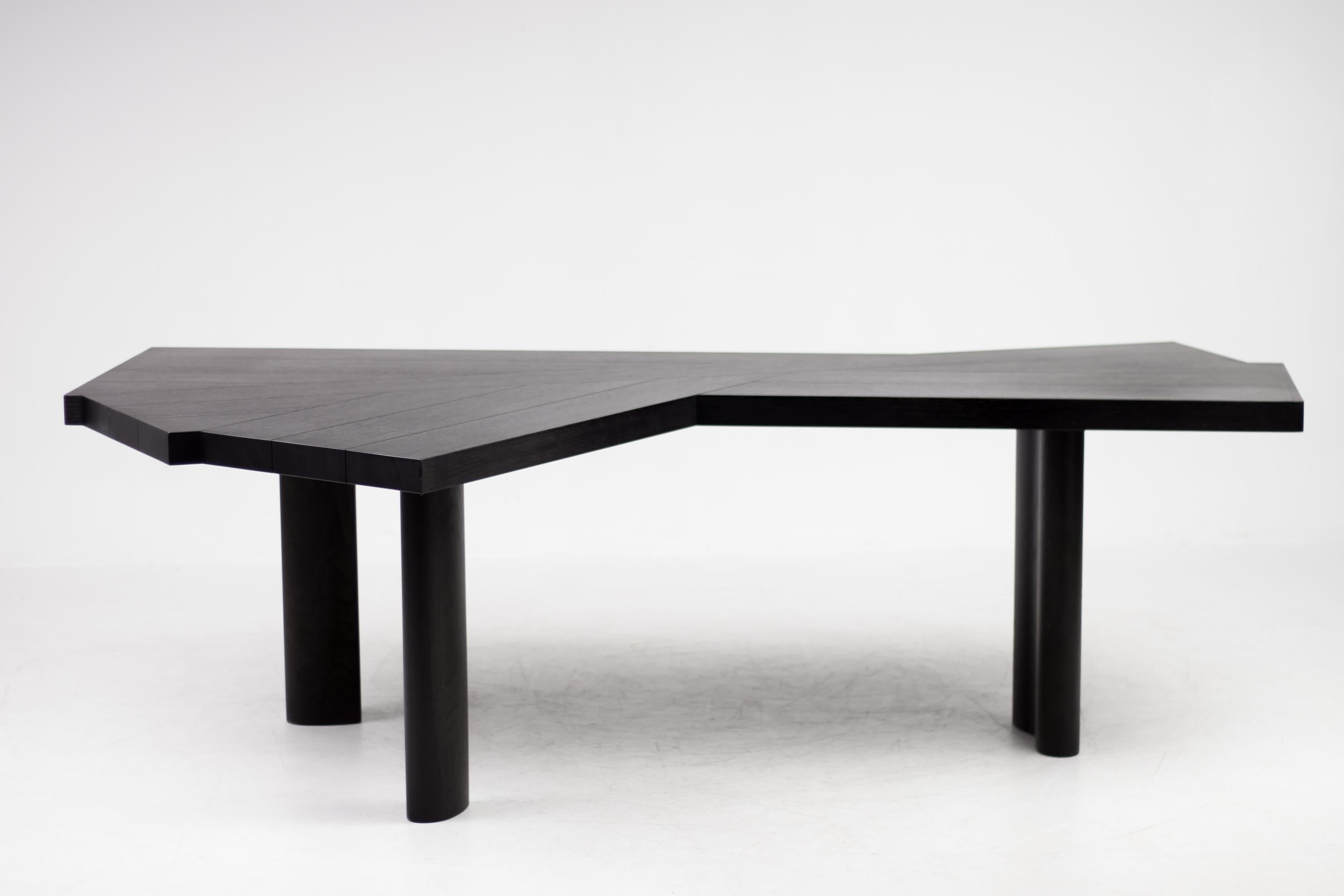 Table in black stained oak. The tabletop is composed of fourteen beams; the base has three legs.
The special configuration of the top and the leg placement allow dynamic and flexible table usage, also by a greater number of persons compared to a