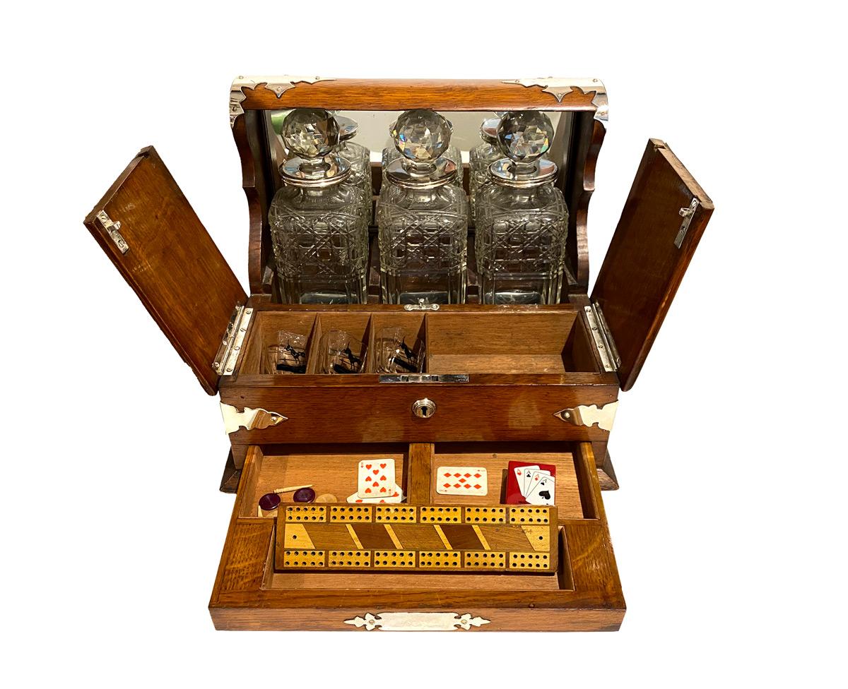 This antique oak Tantalus is enclosing three square-cut crystal spirits decanters within a mirror-back compartment, with their original faceted stoppers and it comes with its key.
An internal compartment reveals 3 shot glasses decorated with a