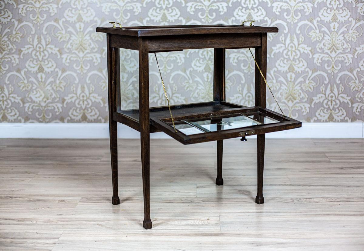 We present you an oak piece of furniture from the early 20th century.
The cabinet is placed on straight, high legs. Its case is glazed and instead of a top, it has a tray.
Furthermore, the front glass is decorated with a handcut pattern.

This