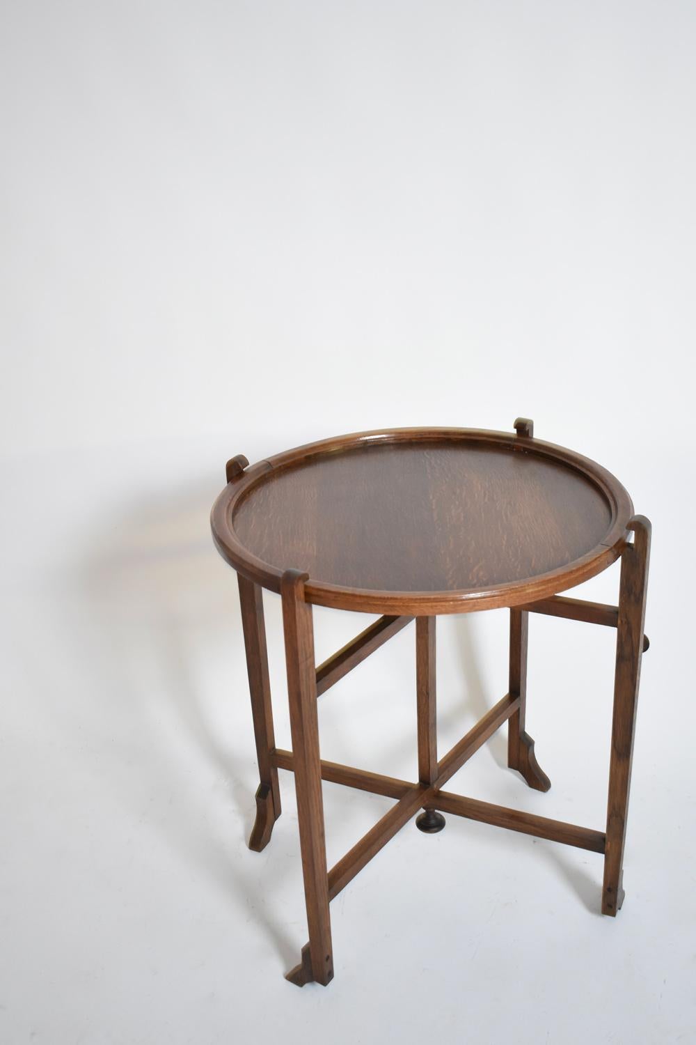 Tavolino da viaggio in rovere tinto Arts & Crafts con base pieghevole cruciforme che sostiene un piano circolare reversibile rivestito in feltro verde. Targa in metallo del produttore (REVERTABLE - BRITISH MADE). Inghilterra, anni '10.