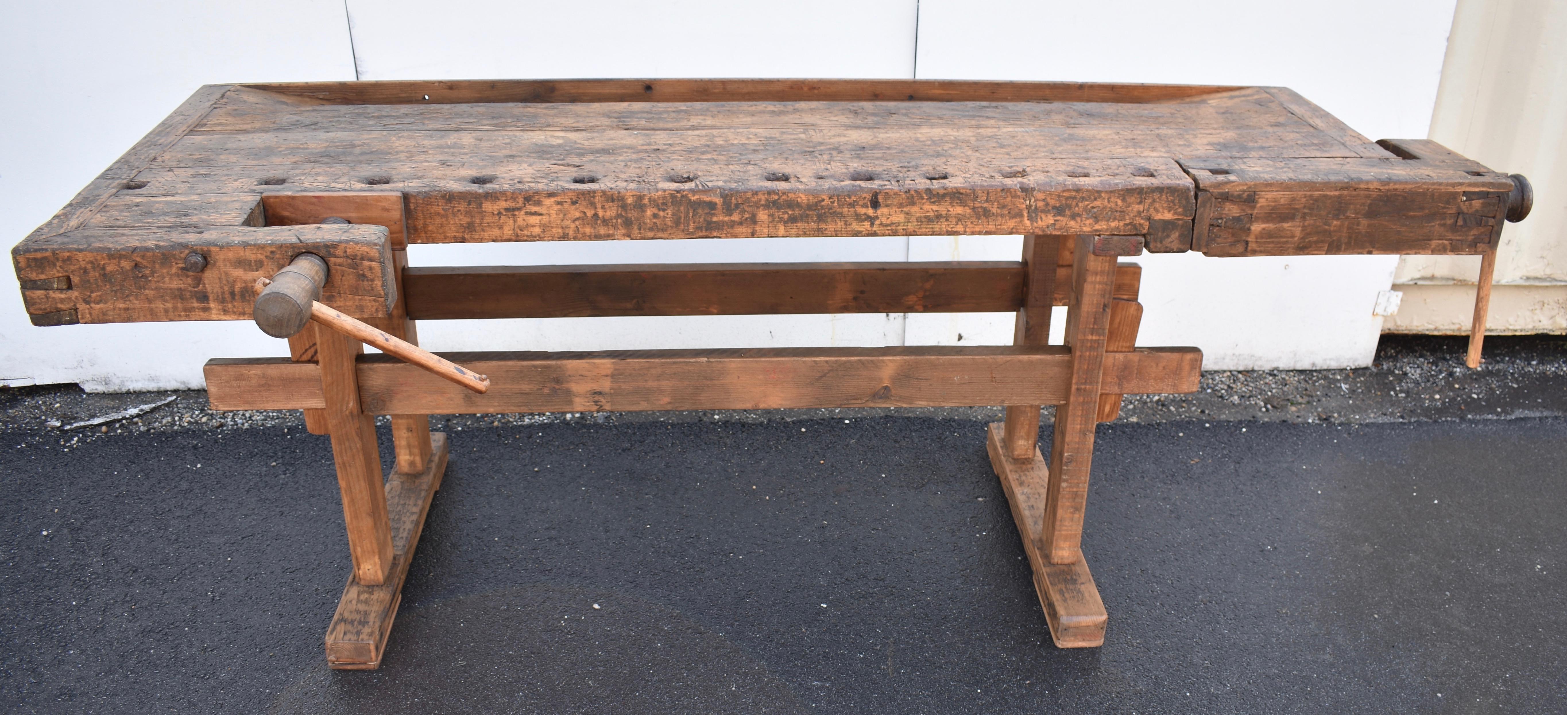 This is a beautifully chopped and gnarled carpenter’s workbench. 
The trestle-style base is made of oak.  The uprights are hand-cut, through-tenoned and pegged top and bottom to the horizontal members. The trestles are joined by two 2”x4”