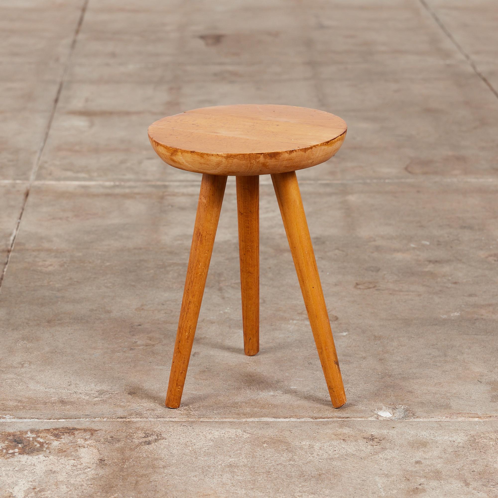 Patinated wooden tripod milking stool. The stool features a thick hand carved rounded seat with visible growth rings, that sits atop three turned wooden legs.

Measurements:
9