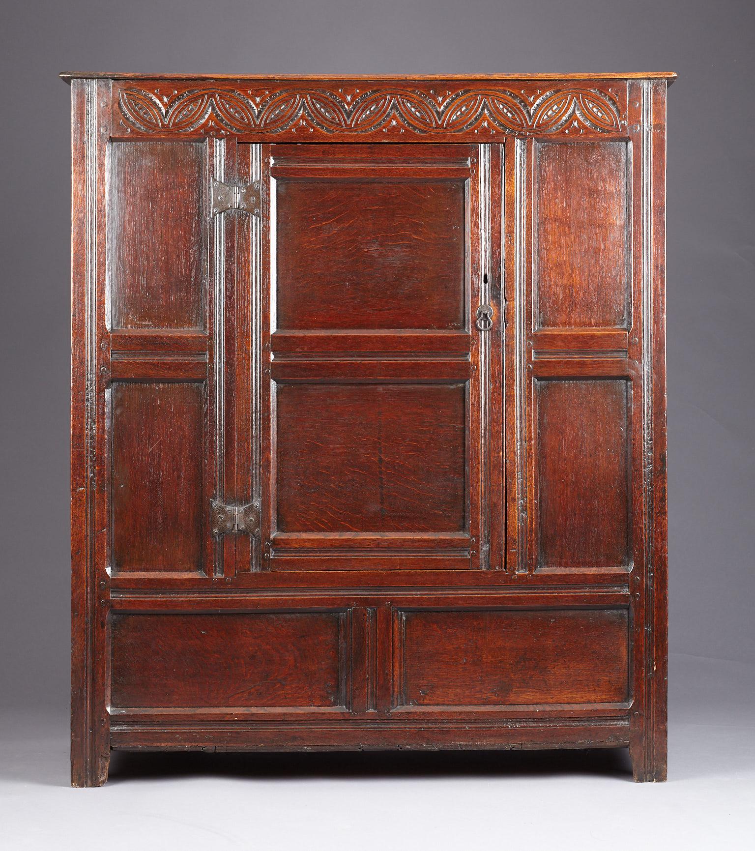 Small Charles II oak wardrobe or clothes press, Lancashire, circa 1670 - 1680.

The panelled cabinet with lunette carved top frieze and single cupboard door with original iron butterfly hinges, flanked by deep moulded framed vertical panels above a