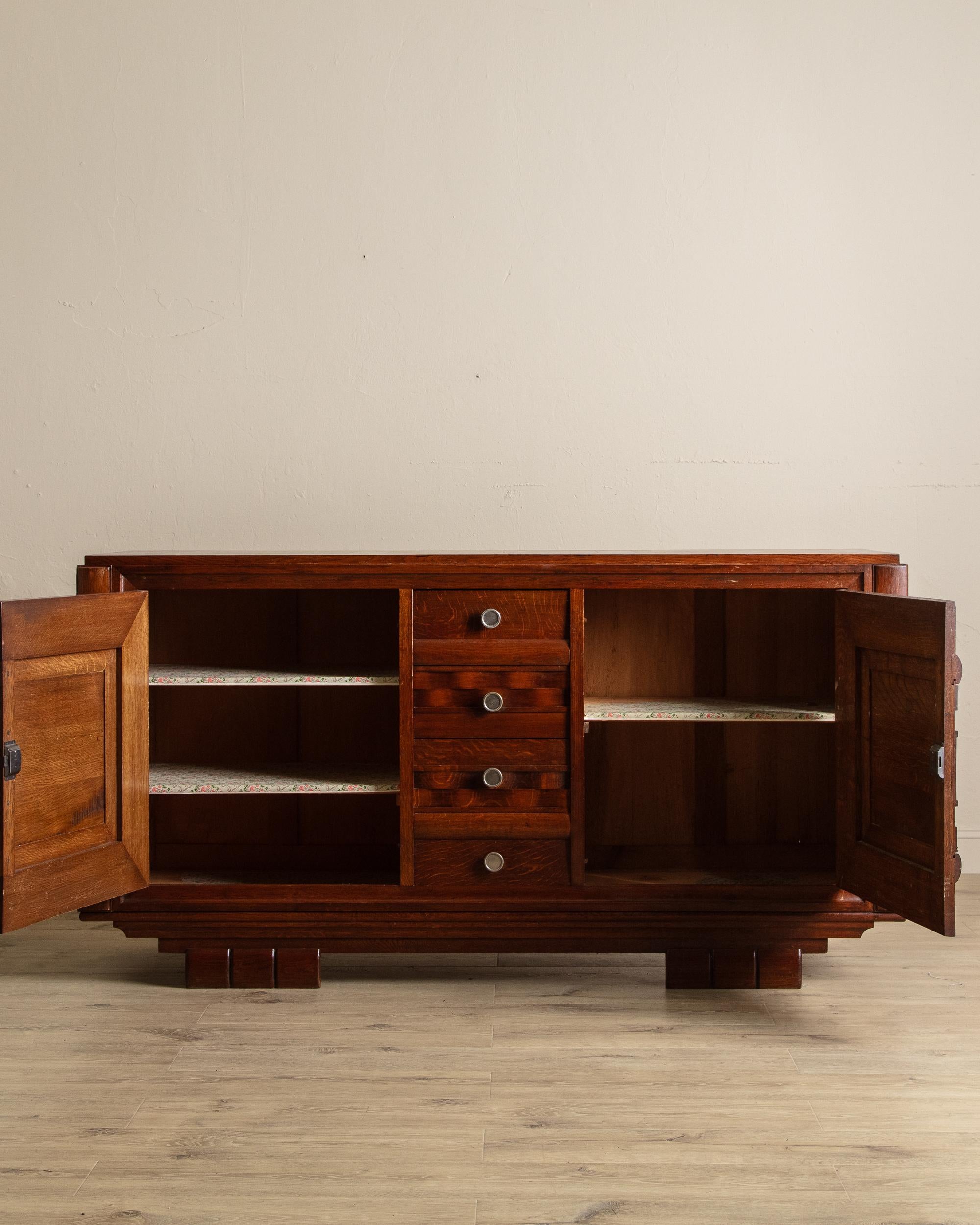 This 1940s French Art Deco sideboard showcases bold craftsmanship with clean geometry and refined detailing. Constructed from richly toned oak, the piece features two large paneled cabinet doors flanking a central bank of four drawers, each accented