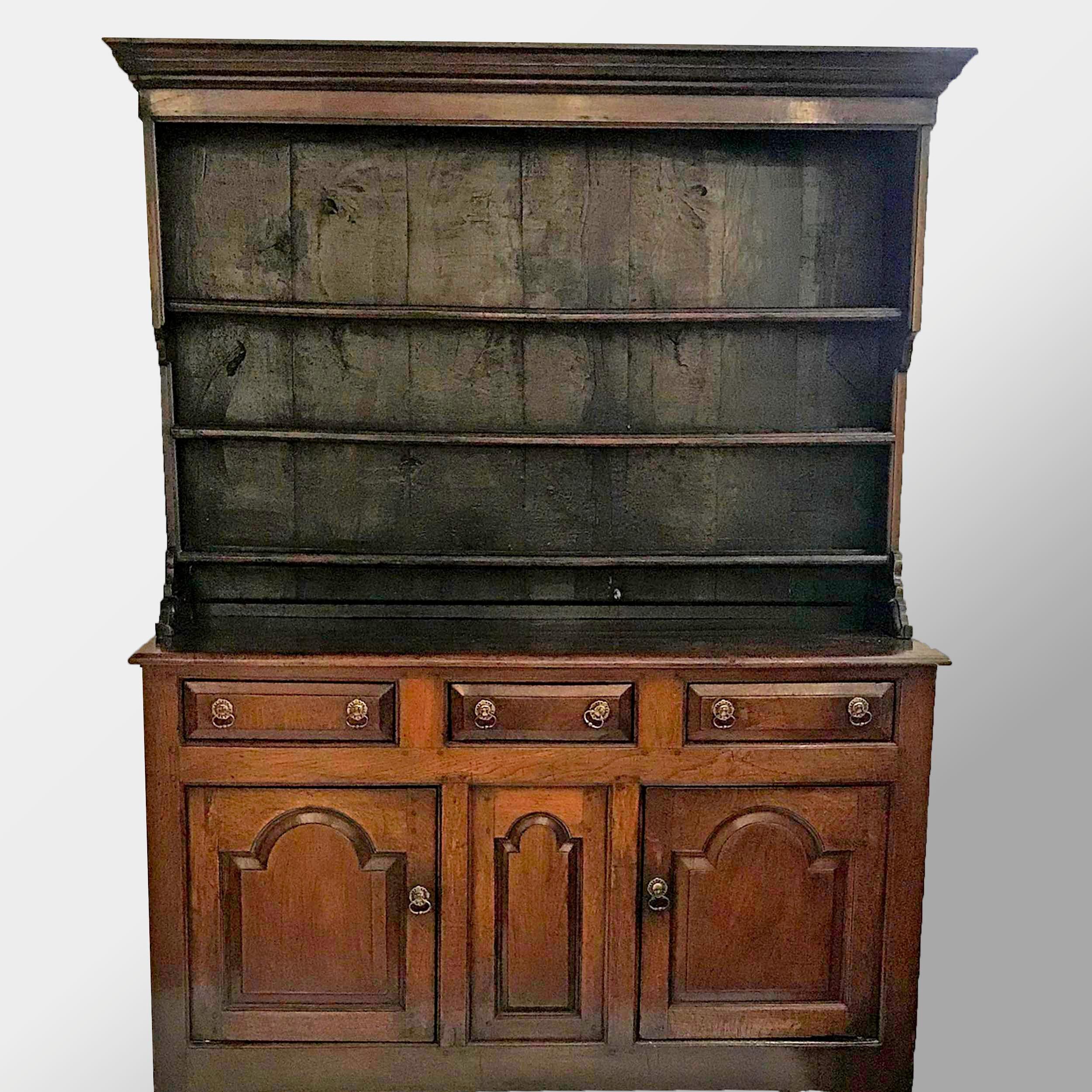 Welsh dresser in two parts. The upper section with a rectangular molded cornice above an open section with three plate racks and notched sides. The lower section with three short drawers above two-paneled arcaded doors and an arcaded center panel.