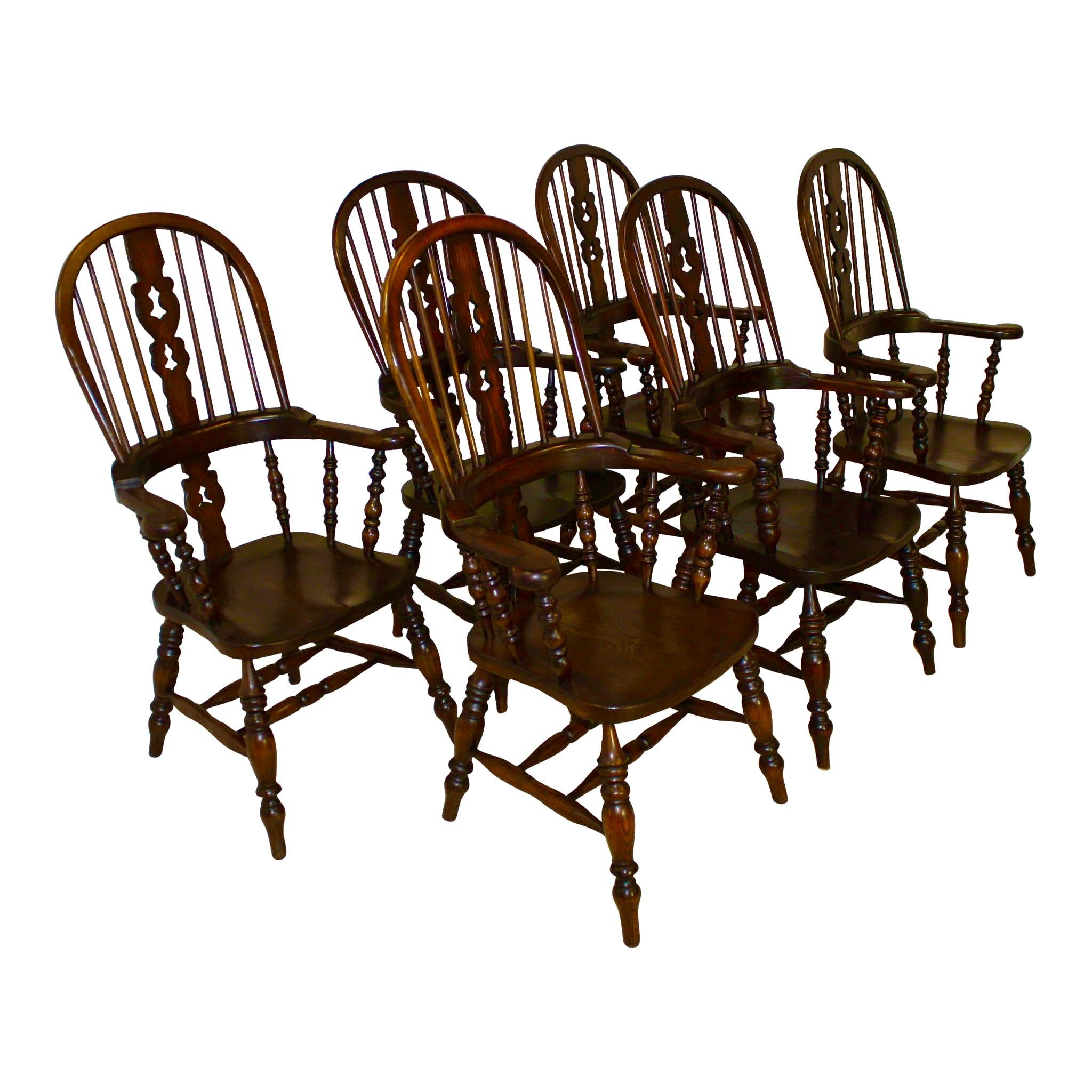 This exceptional set consists of six substantial Windsor armchairs with pierced splat backs, wide arms, and saddle-style seats. Traditional, slender, upper spindles are joined to the high, hooped backs and continuous arm rails. Lower spindles and