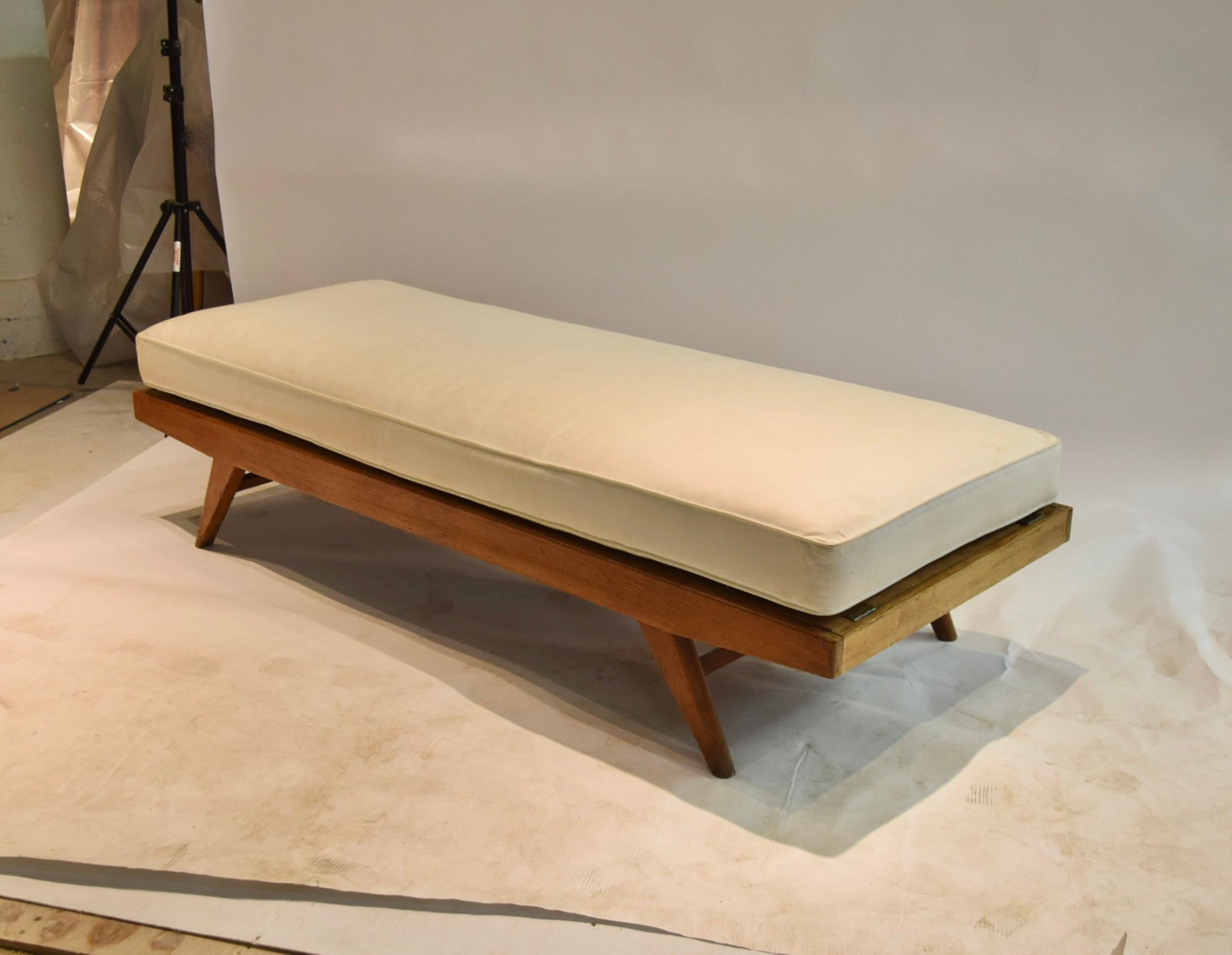 Daybed made by and labeled Free Span made of oakwood with four angled tampered legs, a stretcher at each end, a metal spring support frame located below the flat wooden platform, and a custom cushion upholstered in muslin. 
Listed seat height