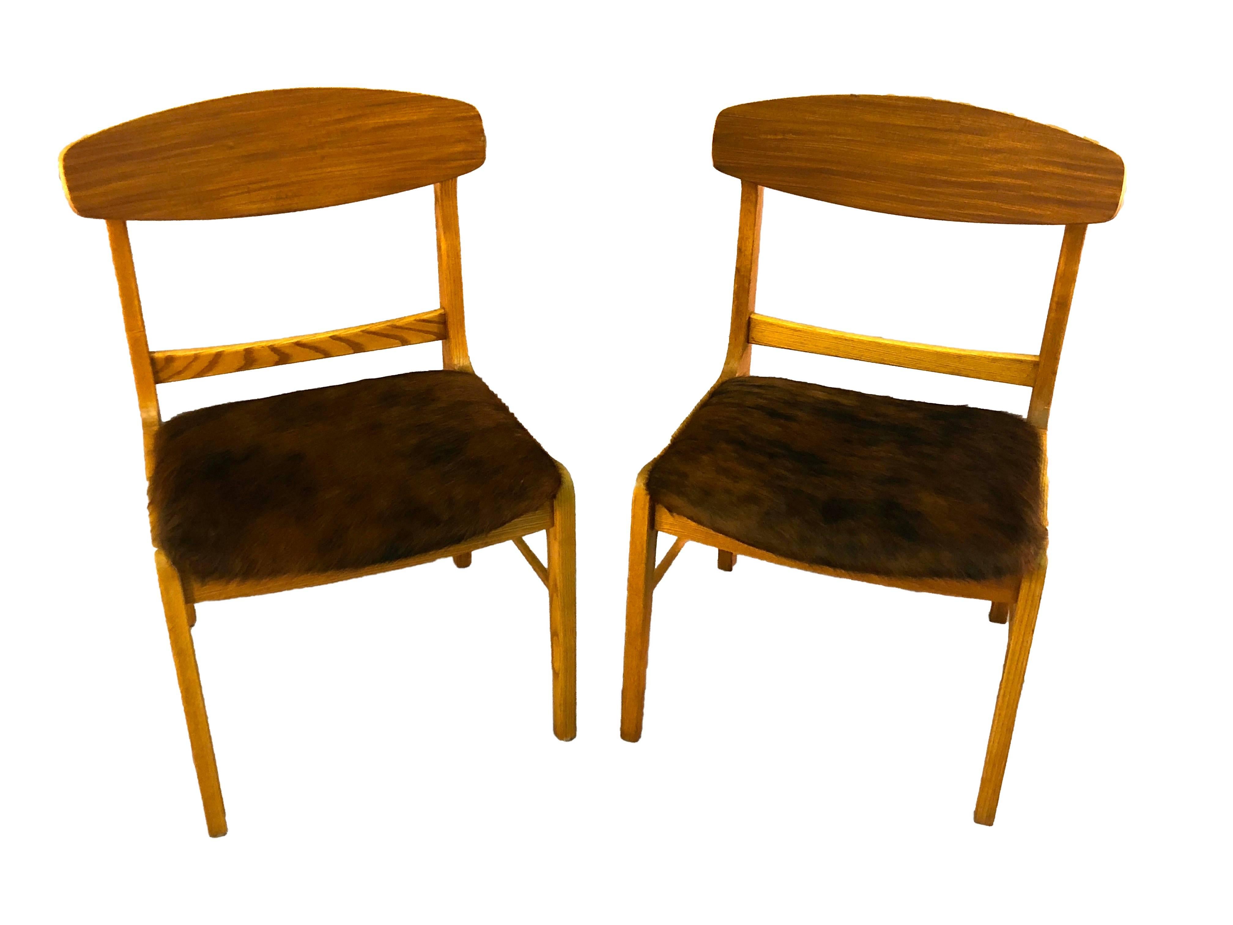 Vintage 1960s pair of oak and teak wood round back dining room chairs with brown cowhide seats. The chairs are in newly refinished condition. Seats, 17in.H. Unmarked.
 