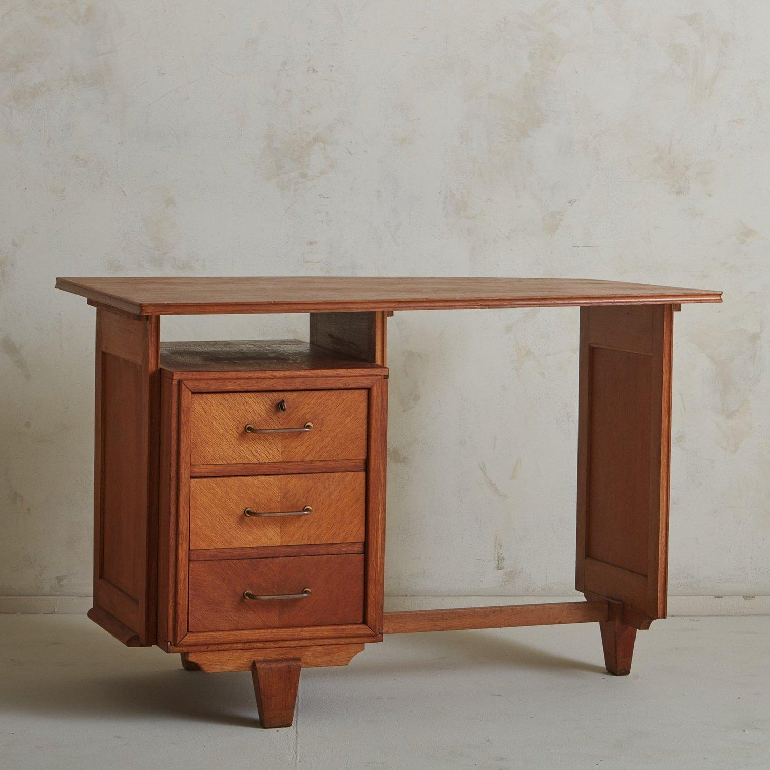 A 1950s French writing desk in the style of French design duo Guillerme et Chambron. This desk was beautifully constructed using oak with gorgeous wood graining and carved detailing. It has three drawers, the front of which feature a subtle