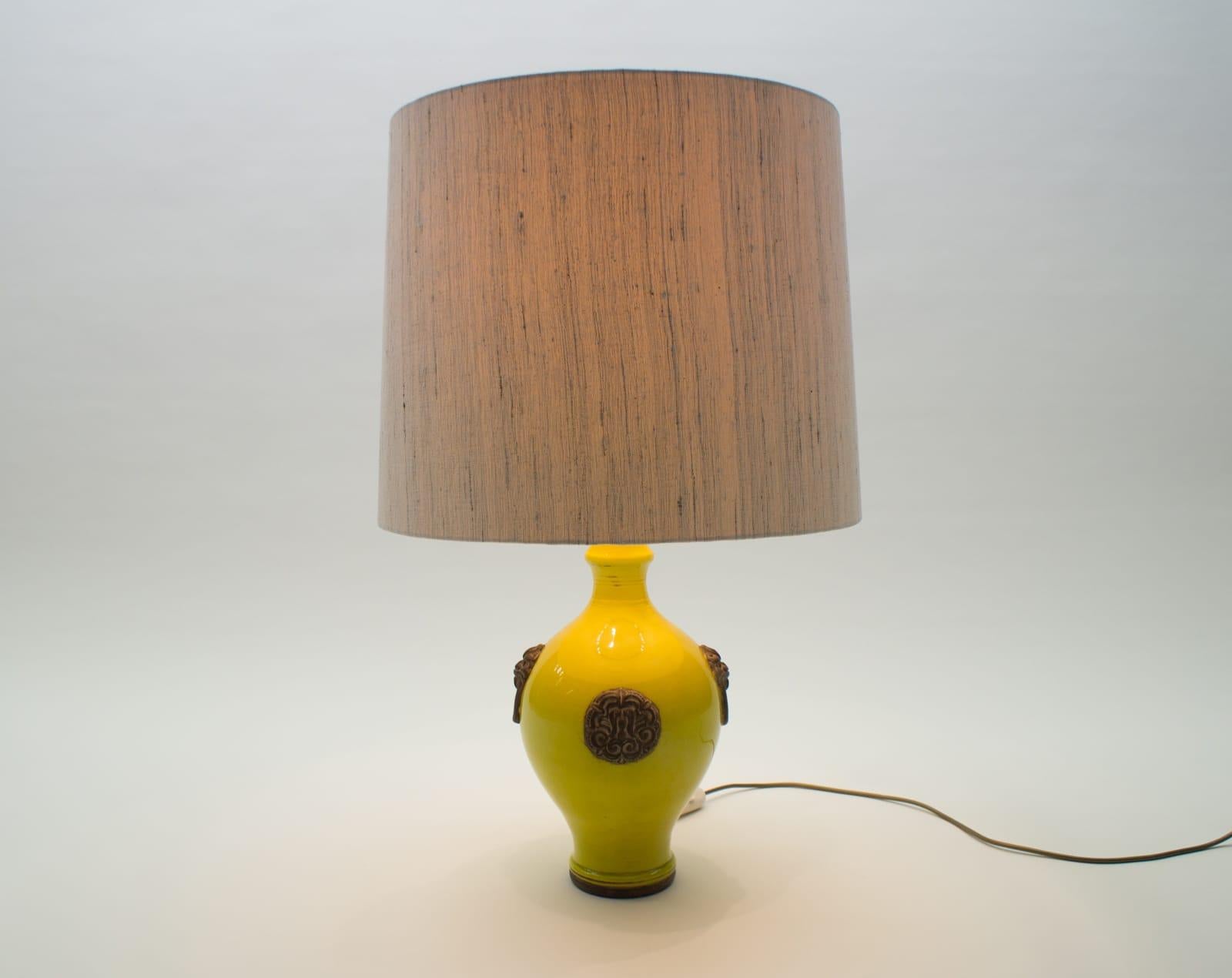 Great strong yellow. In beautiful contrast to the brown appliqués. With original lampshade. 

A fine ceramic table lamp in an ovoid form with a double waisted flared neck and flanked on four sides by animal masks with mock ring handles in a gilt