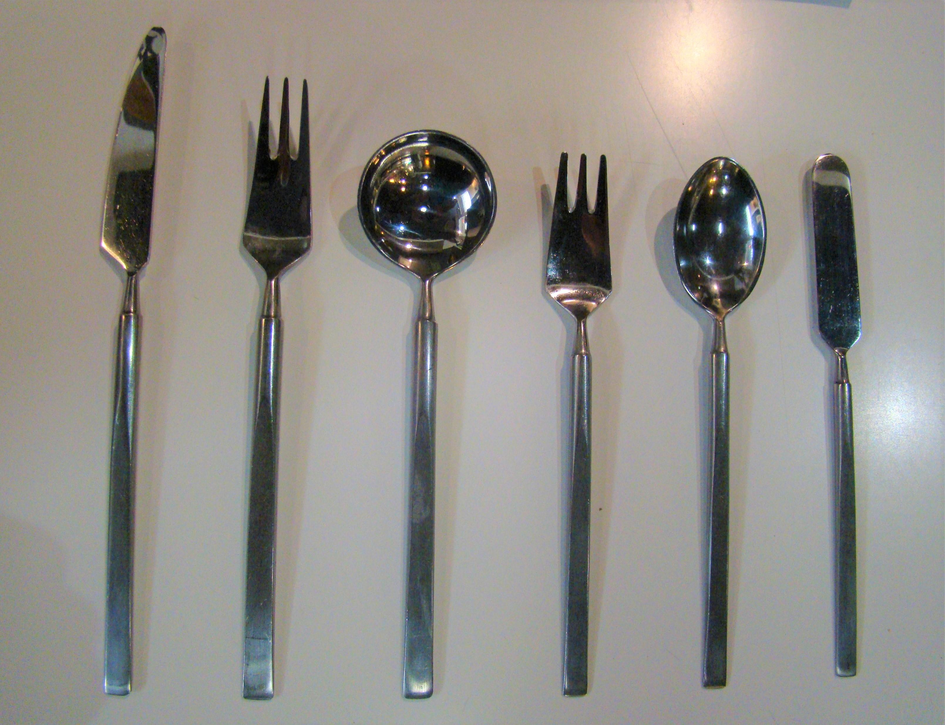 Eight vintage, six piece place settings of the iconic Obelisk pattern (design. 1954) by Erik Herlow in stainless steel, complete with original gift boxes. Includes serving fork and serving spoon. Very nice vintage condition. Complete set, never used