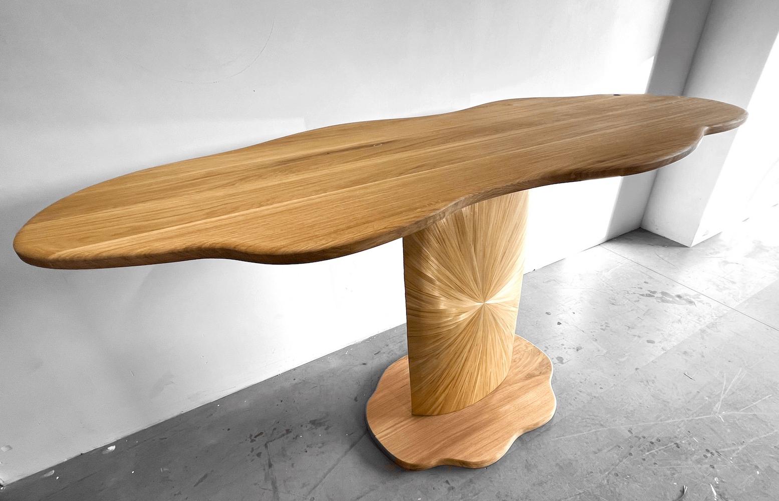 Oblivion, a cloud-shaped high table, has been crafted completely by hand and draws its inspiration from the village of Saint-Tropez. The warmth of the light oak wood and the shimmering chatoyance of the straw marquetry are reminiscent of the